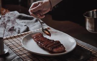 A stylish plated cooked cut of venison, being drizzled with sauce