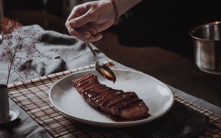 A stylish plated cooked cut of venison, being drizzled with sauce