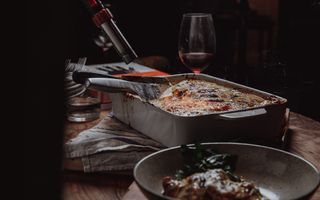 Venison Lasagne ready to be served, alongside a glass of red wine