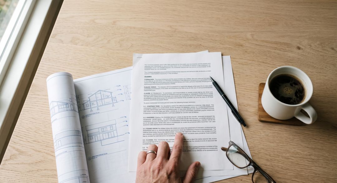 Homeowner reading a written home improvement contract at a kitchen table beside printed construction plans