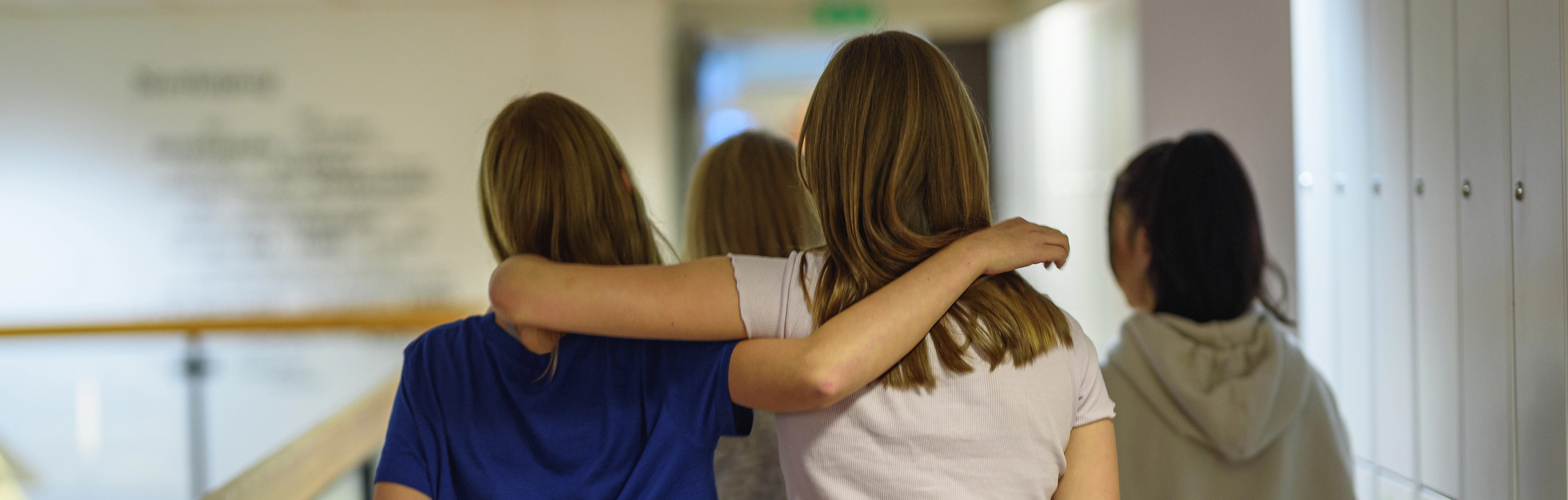 Tjejer håller varandra runt axlarna i skolkorridor