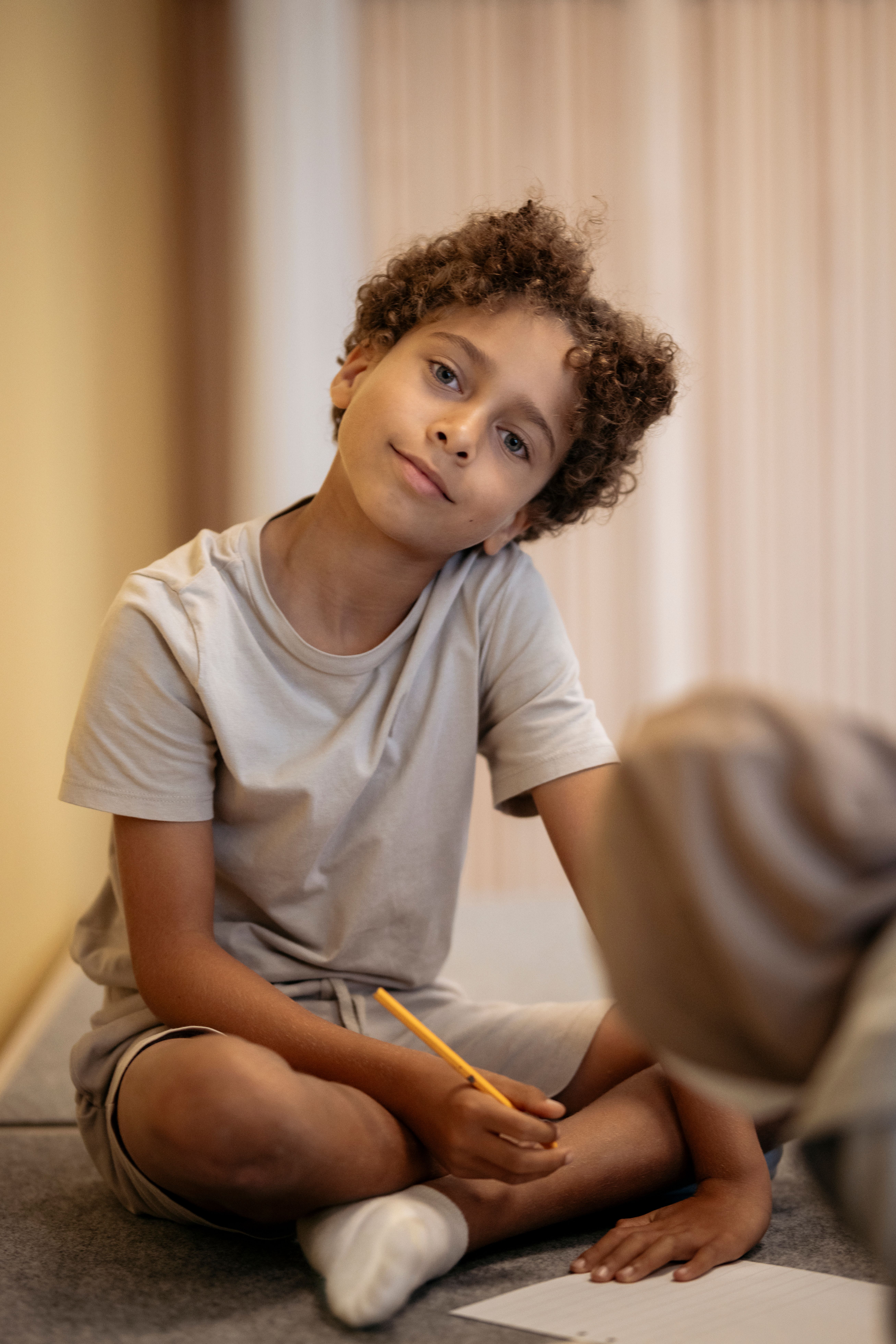 Pojke med lockigt hår och grå tshrirt sitter skräddare och skriver på en uppgift