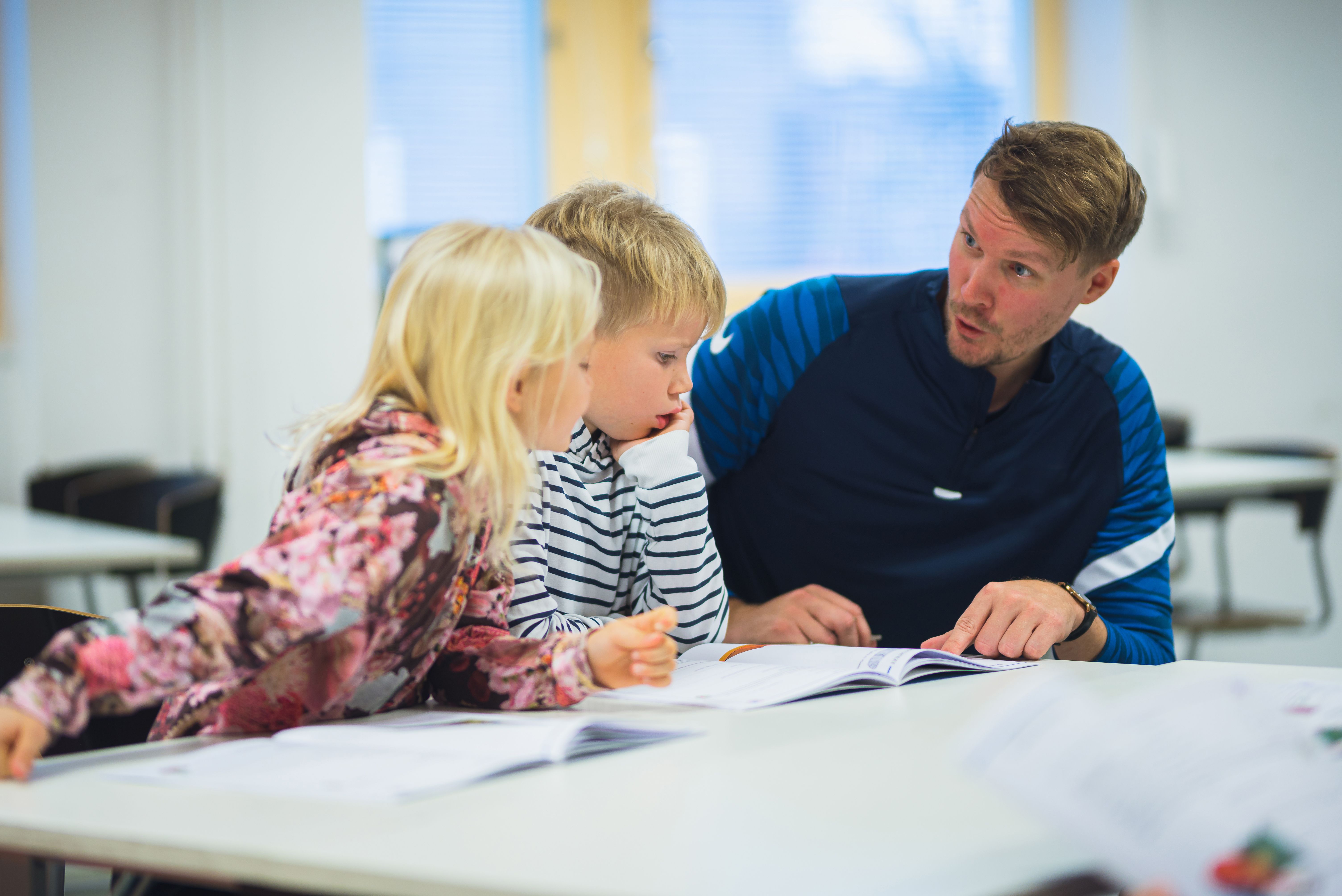 Två elever sitter med sin lärare vid ett bord och pratar