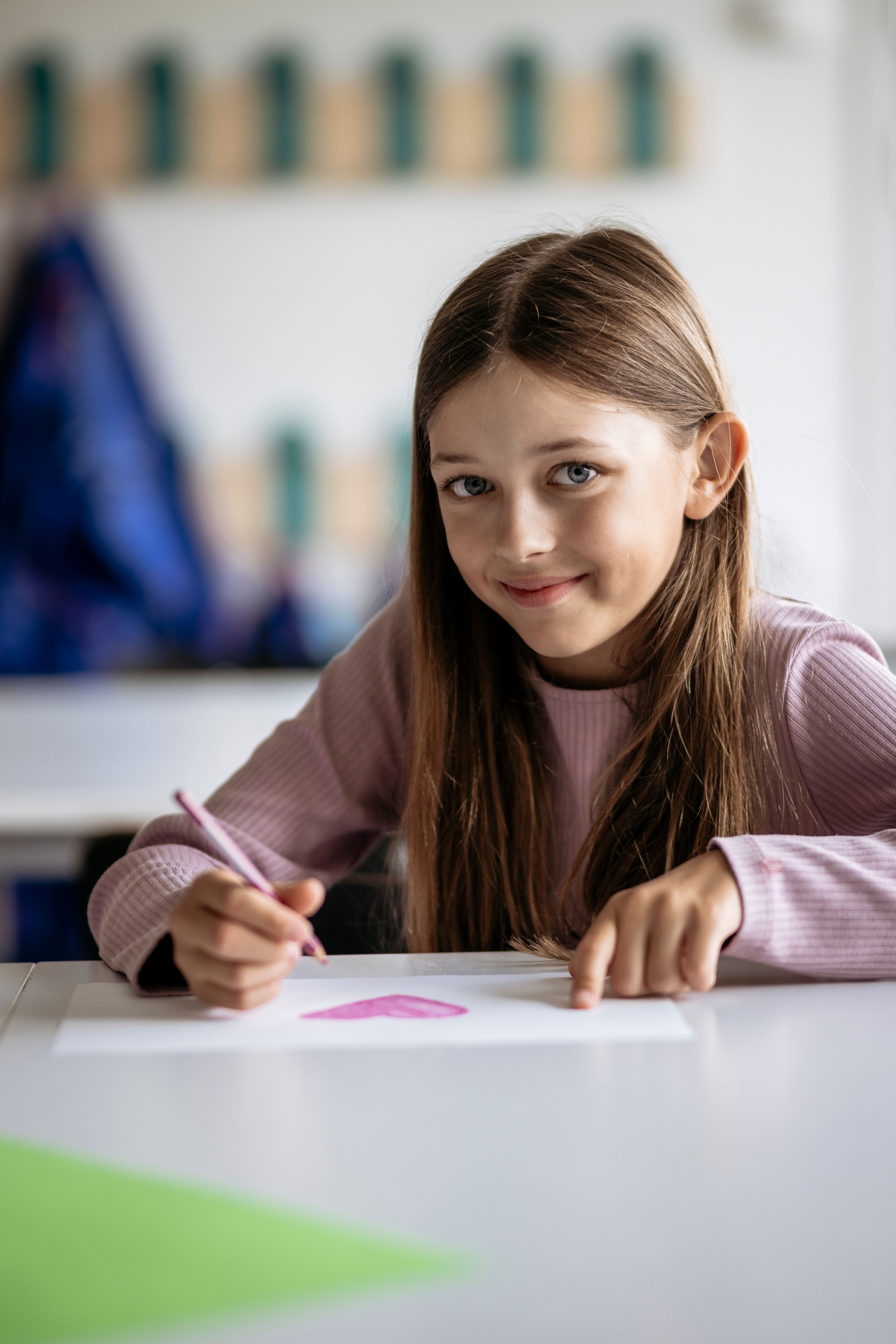 Flicka skriver på papper och ler mot kameran