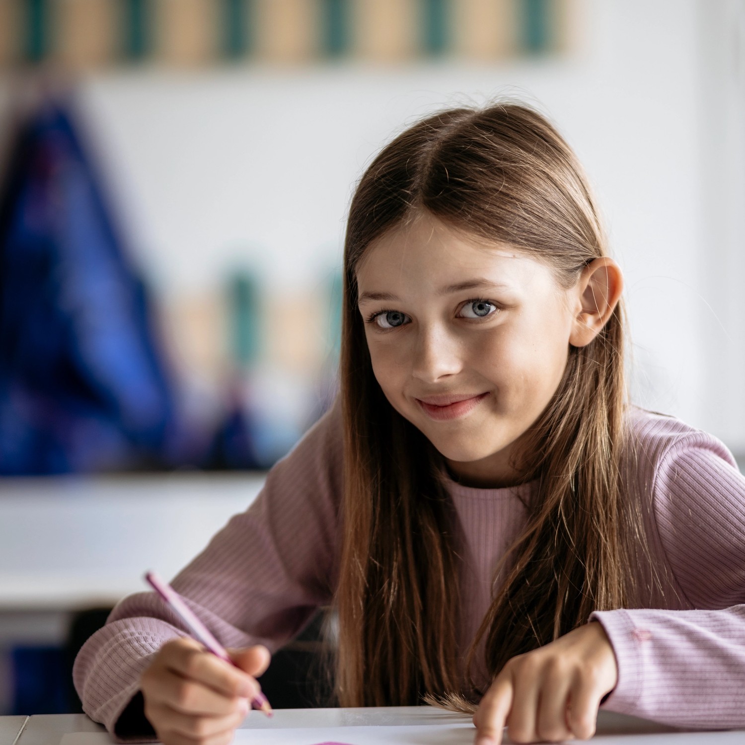 Flicka skriver på papper och ler mot kameran