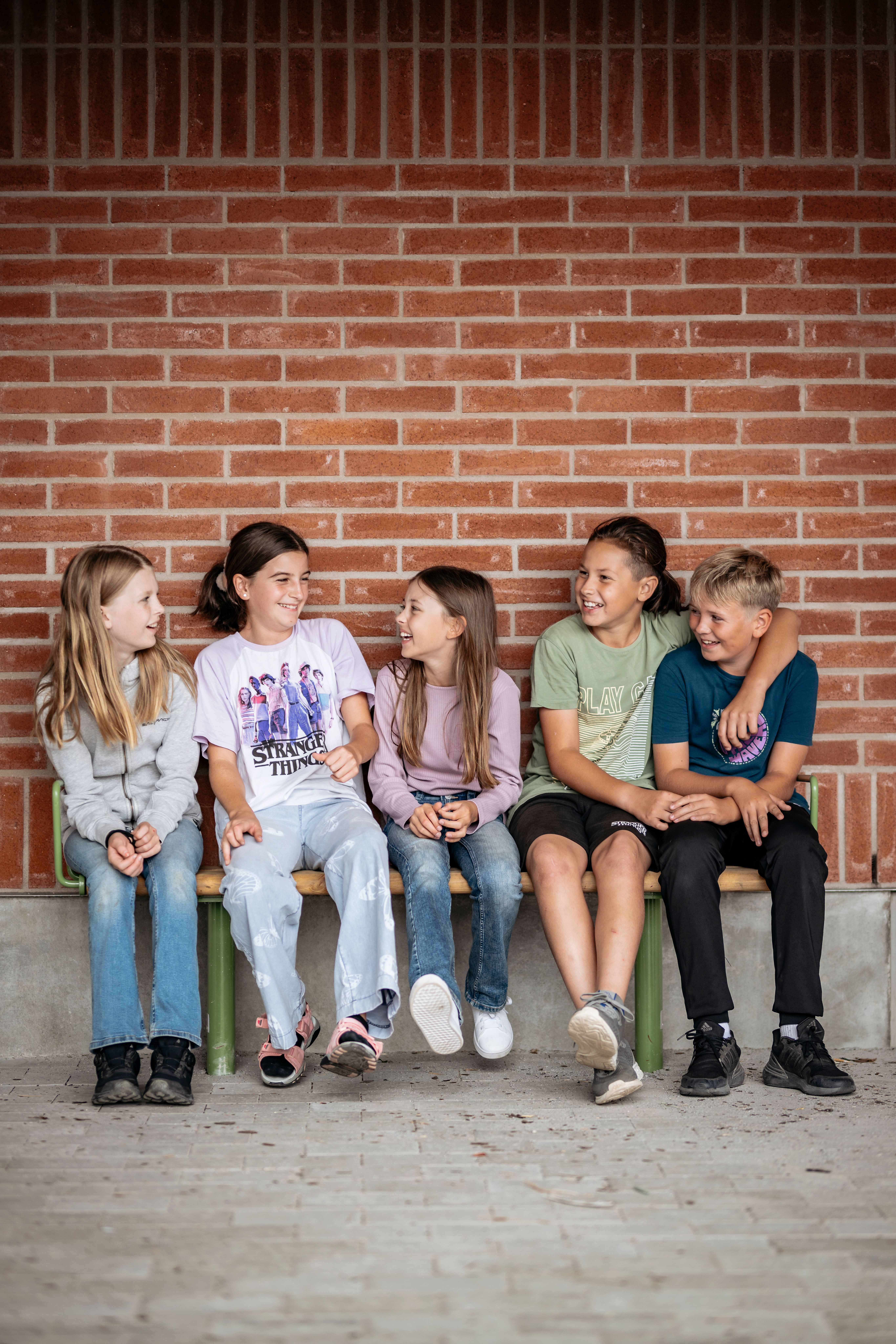 Barn sitter på en bänk mot en tegelvägg