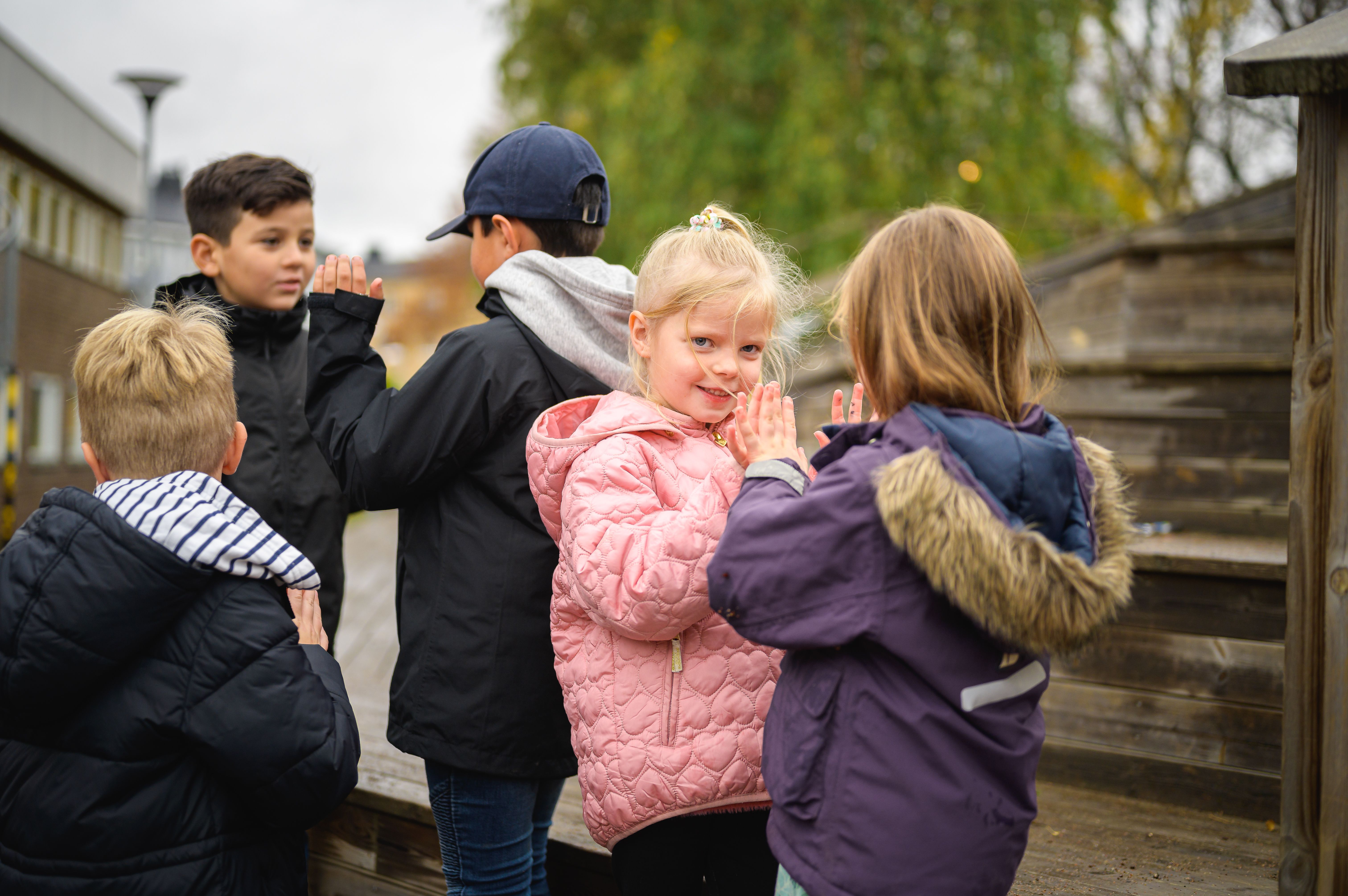 Två mindre flickor leker tillsammans och två äldre pojkar står i bakgrunden