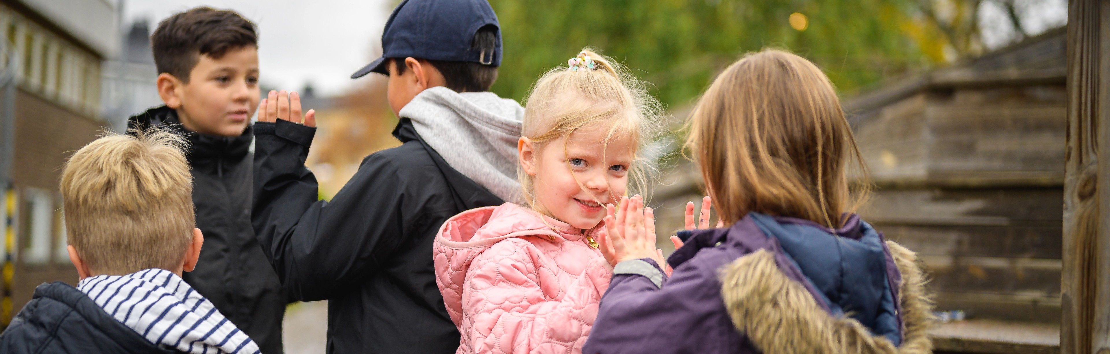 Två mindre flickor leker tillsammans och två äldre pojkar står i bakgrunden