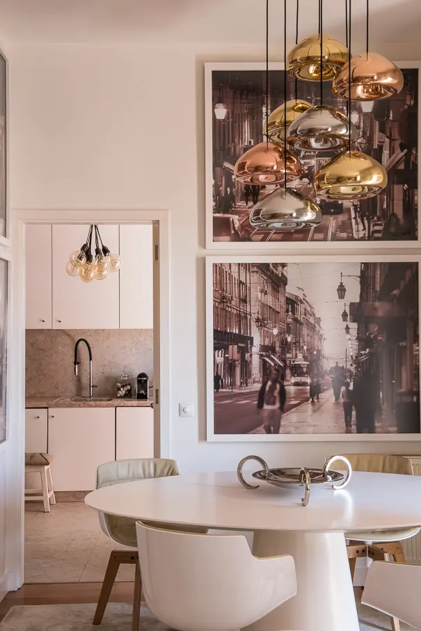 Sala de jantar contemporânea em apartamento no Chiado, Lisboa, com mesa branca oval, iluminação suspensa metálica e fotografias urbanas em grande formato.