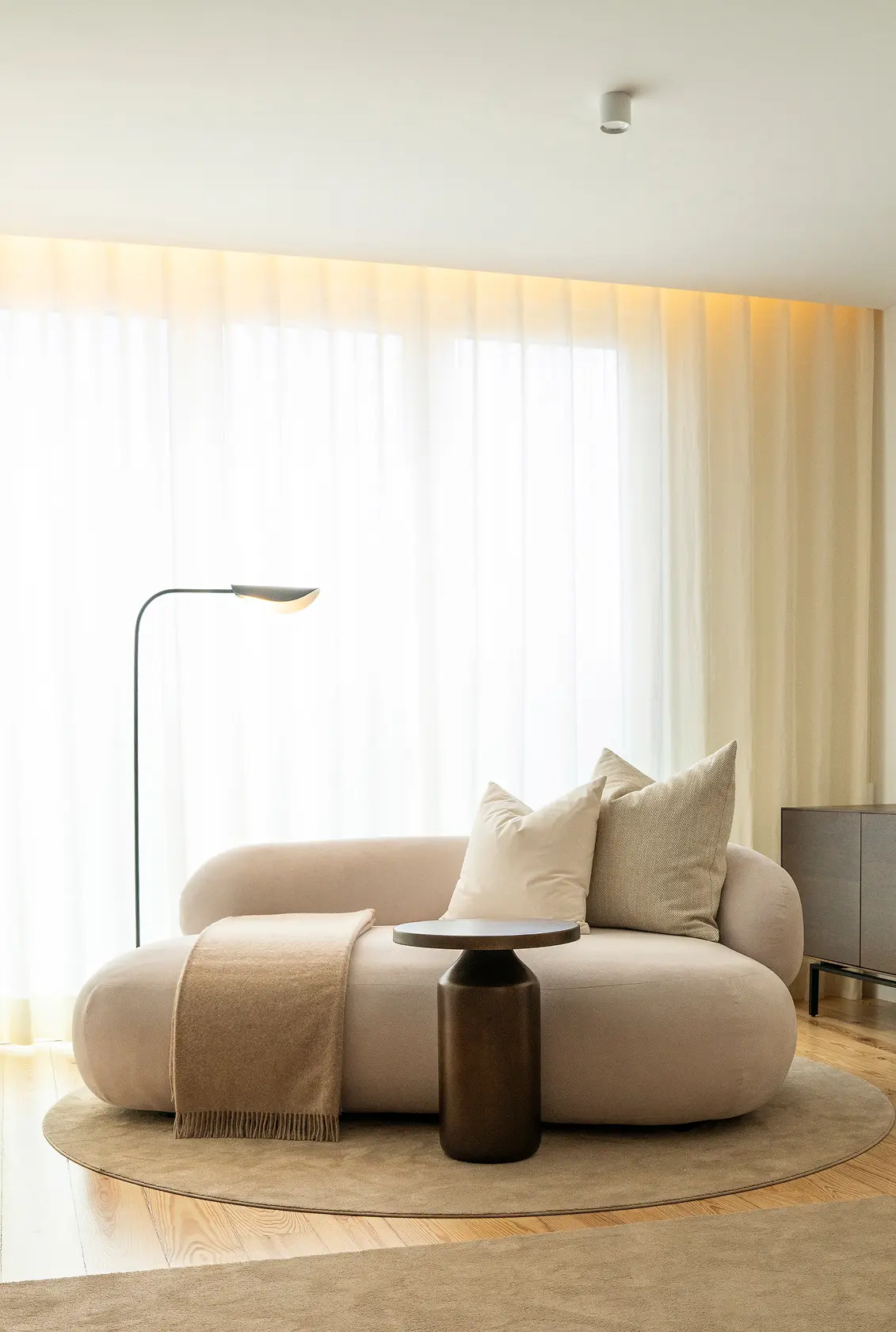 Curved organic beige sofa, round bronze pedestal side table and black arched floor lamp — luxury décor details