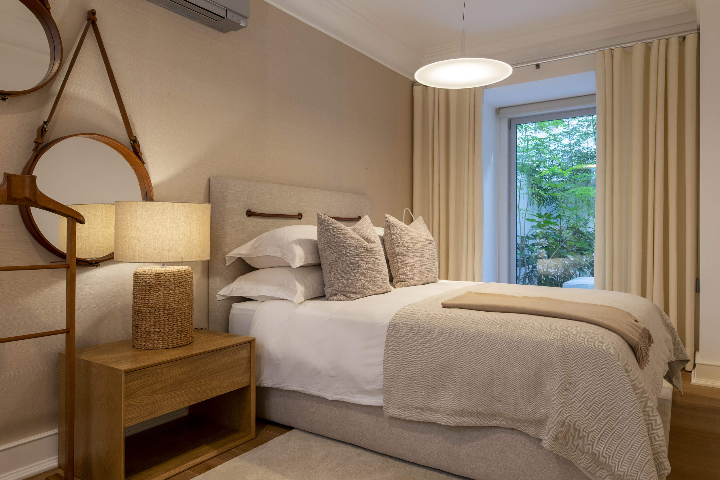 Upholstered headboard with leather straps, round hanging mirror and woven rope table lamp — luxury master suite design