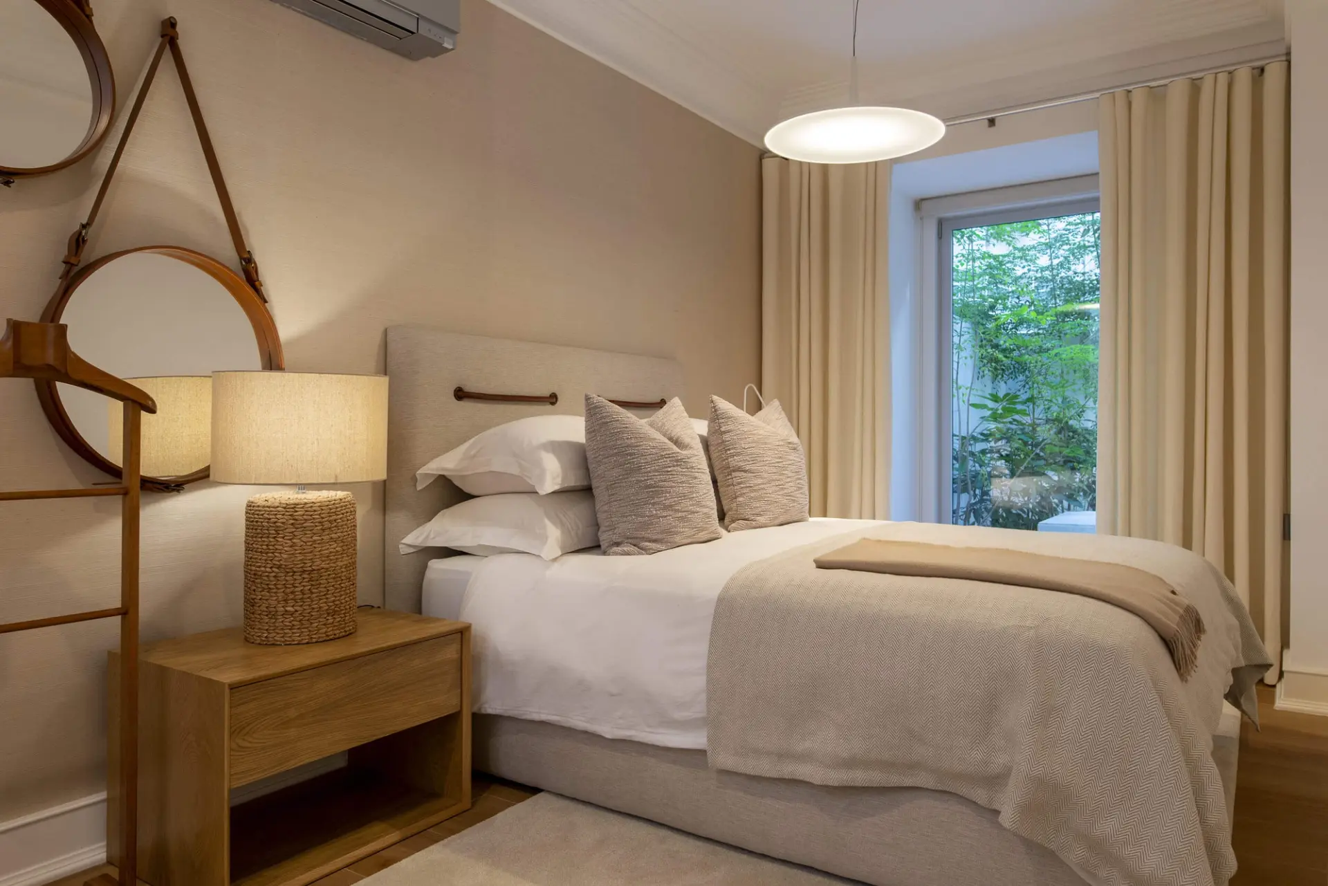 Upholstered headboard with leather straps, round hanging mirror and woven rope table lamp — luxury master suite design