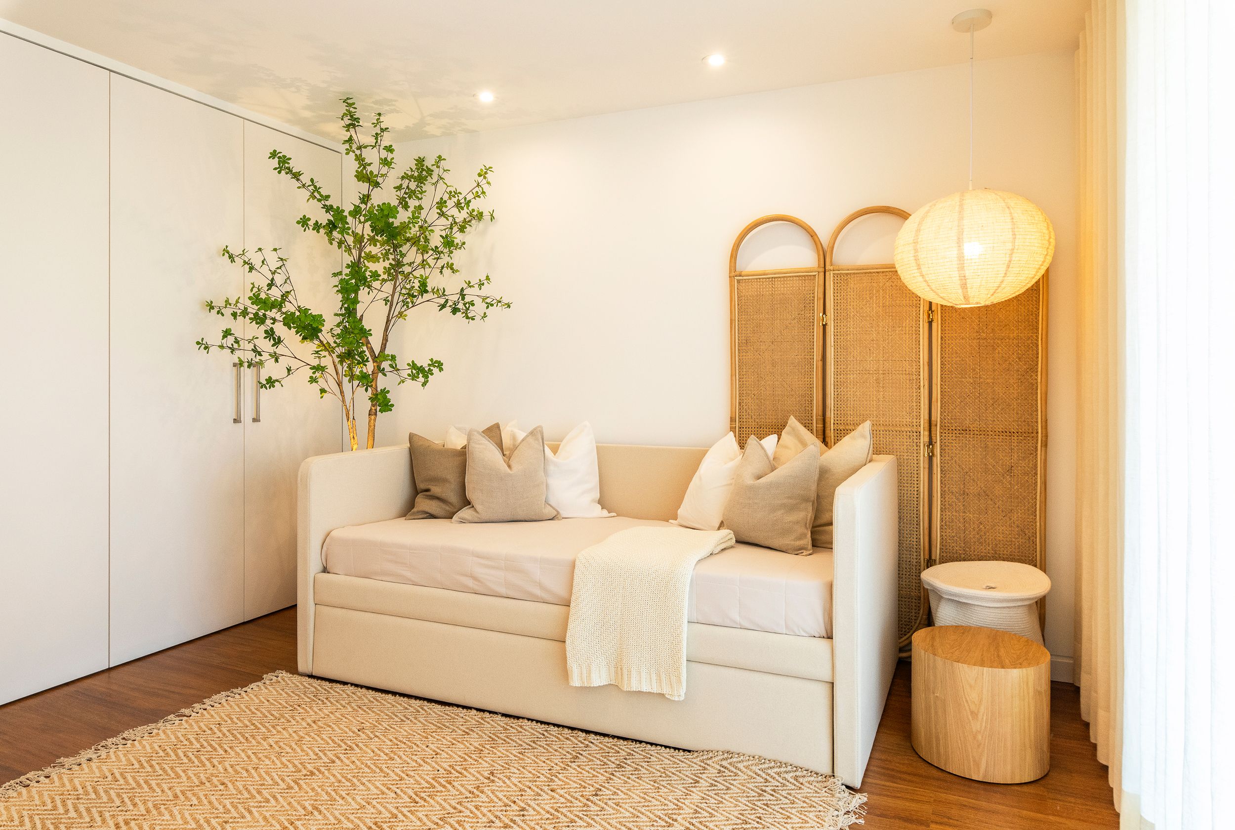 Cama individual estofada com almofadas, biombo arqueado em rattan e suspensão globo em papel — quarto jovem de luxo