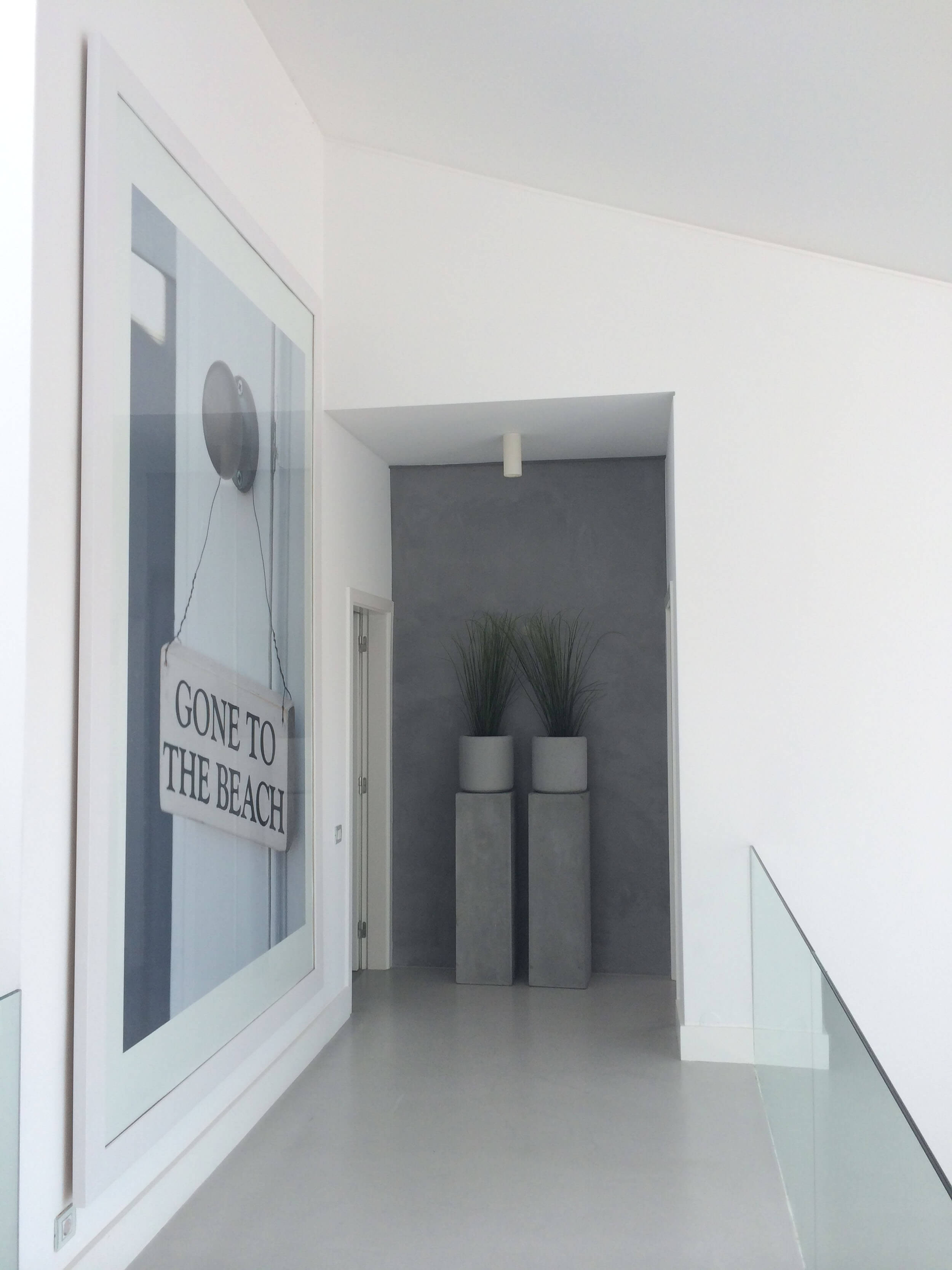 Corredor branco com quadro decorativo, vasos altos em betão e guarda em vidro — design de interiores de luxo Tróia, Setúbal