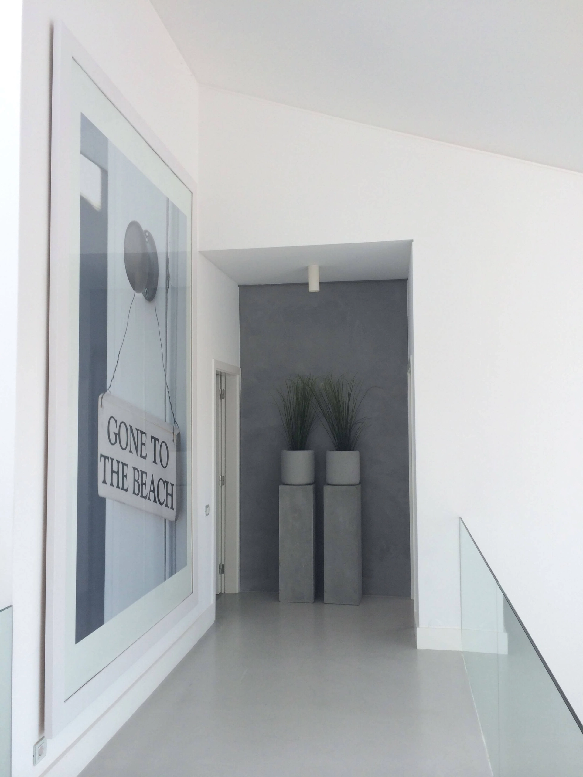 Corredor branco com quadro decorativo, vasos altos em betão e guarda em vidro — design de interiores de luxo Tróia, Setúbal