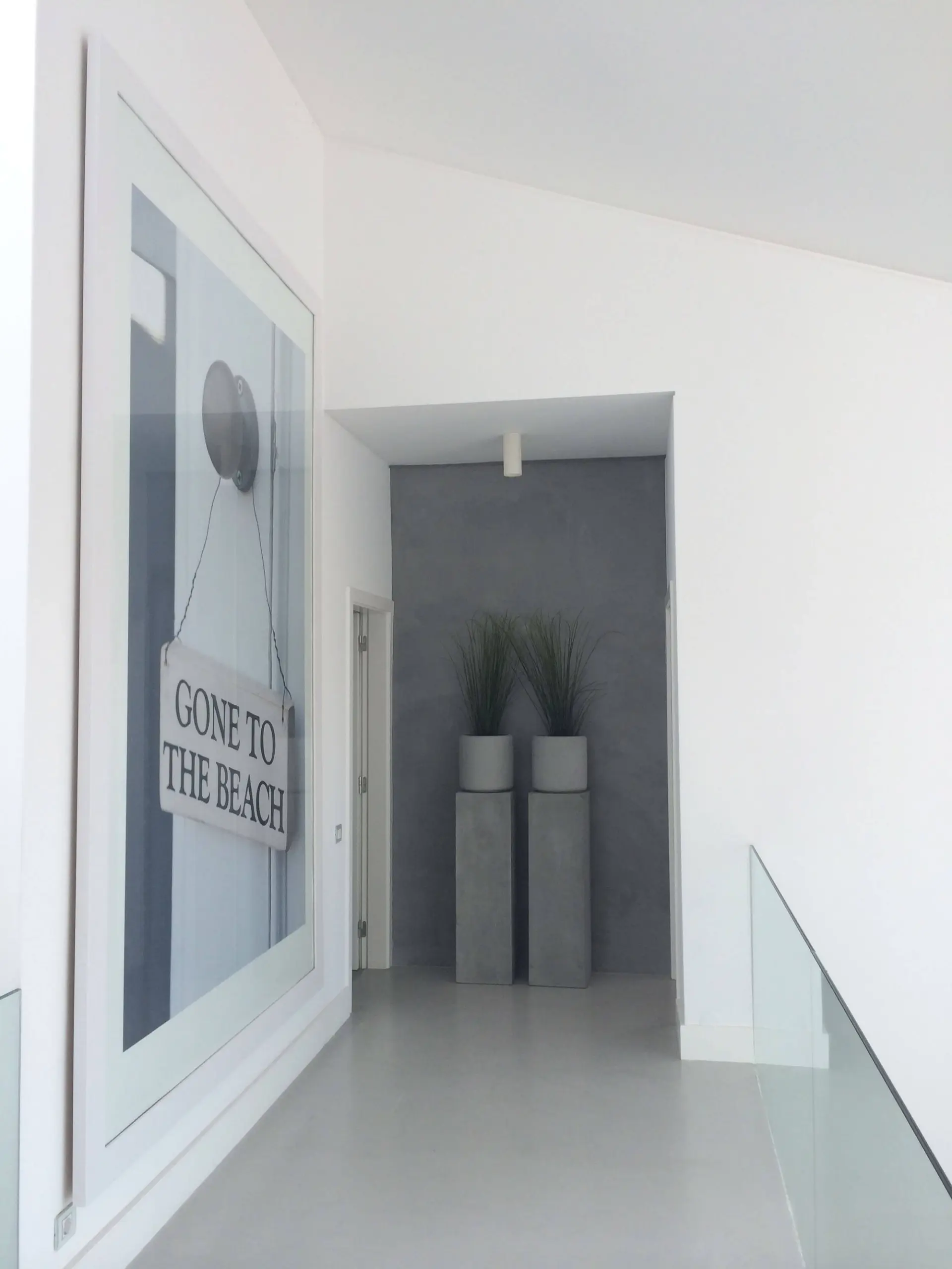 Corredor branco com quadro decorativo, vasos altos em betão e guarda em vidro — design de interiores de luxo Tróia, Setúbal