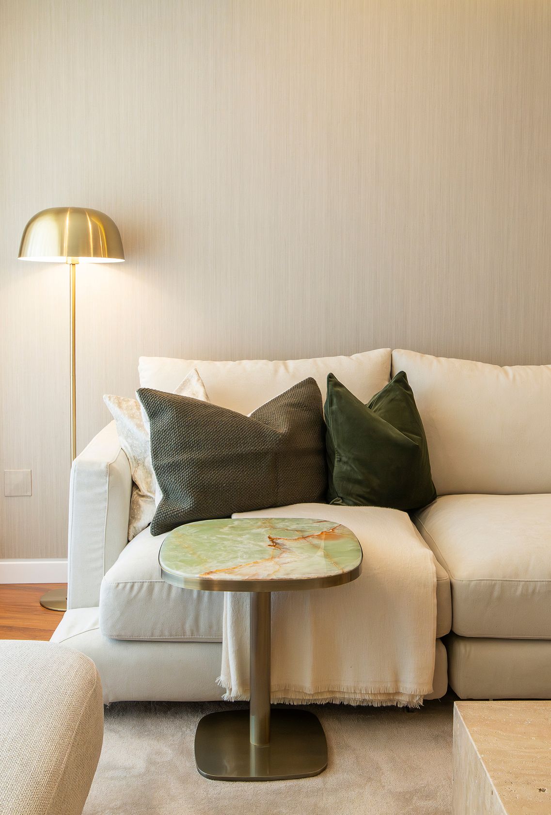 Detalhe de decoração de apartamento com sofá claro, almofadas decorativas e mesa lateral em pedra