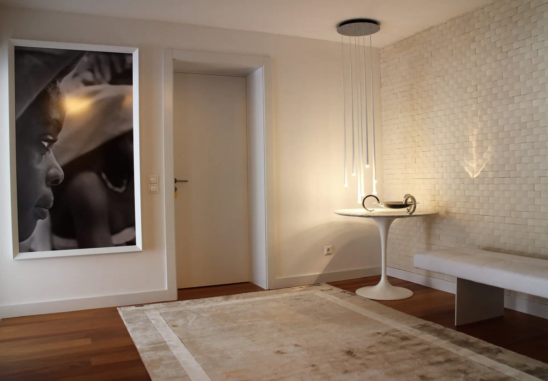 Large-format portrait photograph, white tulip pedestal table and a cascade of slender pendant lights — luxury entrance hall