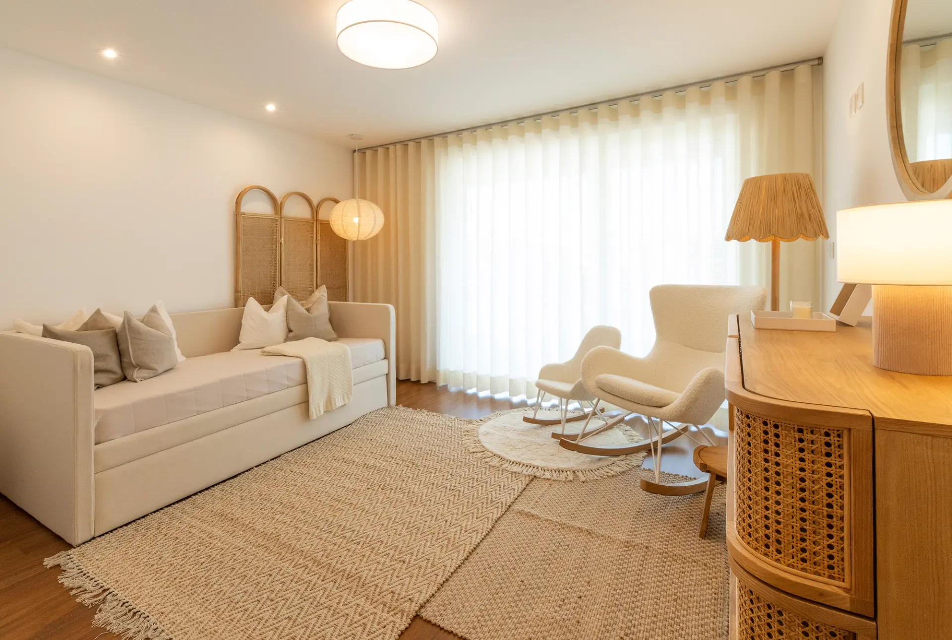 Cama individual estofada branca, cadeiras de baloiço em bouclé e cómoda de palhinha com biombo em rattan — quarto de bebé de luxo