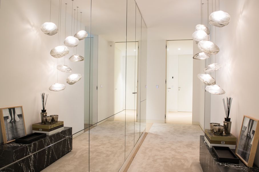 Hall de entrada com parede espelhada, candeeiros suspensos e móvel baixo em pedra escura, num projeto do Atelier Renata Santos Machado.