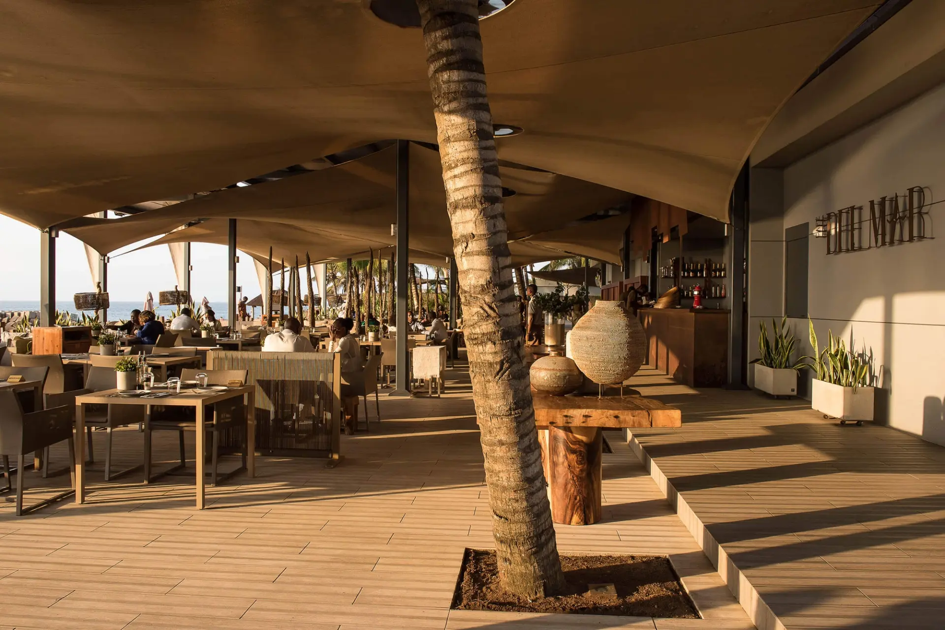 Zona de refeições coberta com toldos drapeados, palmeira e vista mar — design de interiores de restaurante de luxo Luanda, Angola