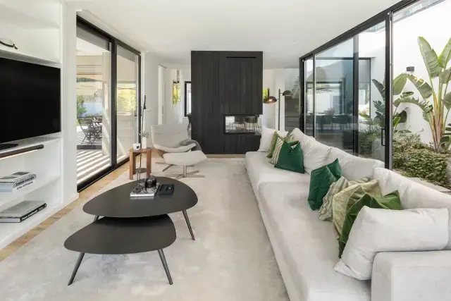 Living room with a white sofa, green accent pillows, nesting coffee tables, and floor-to-ceiling glass doors.