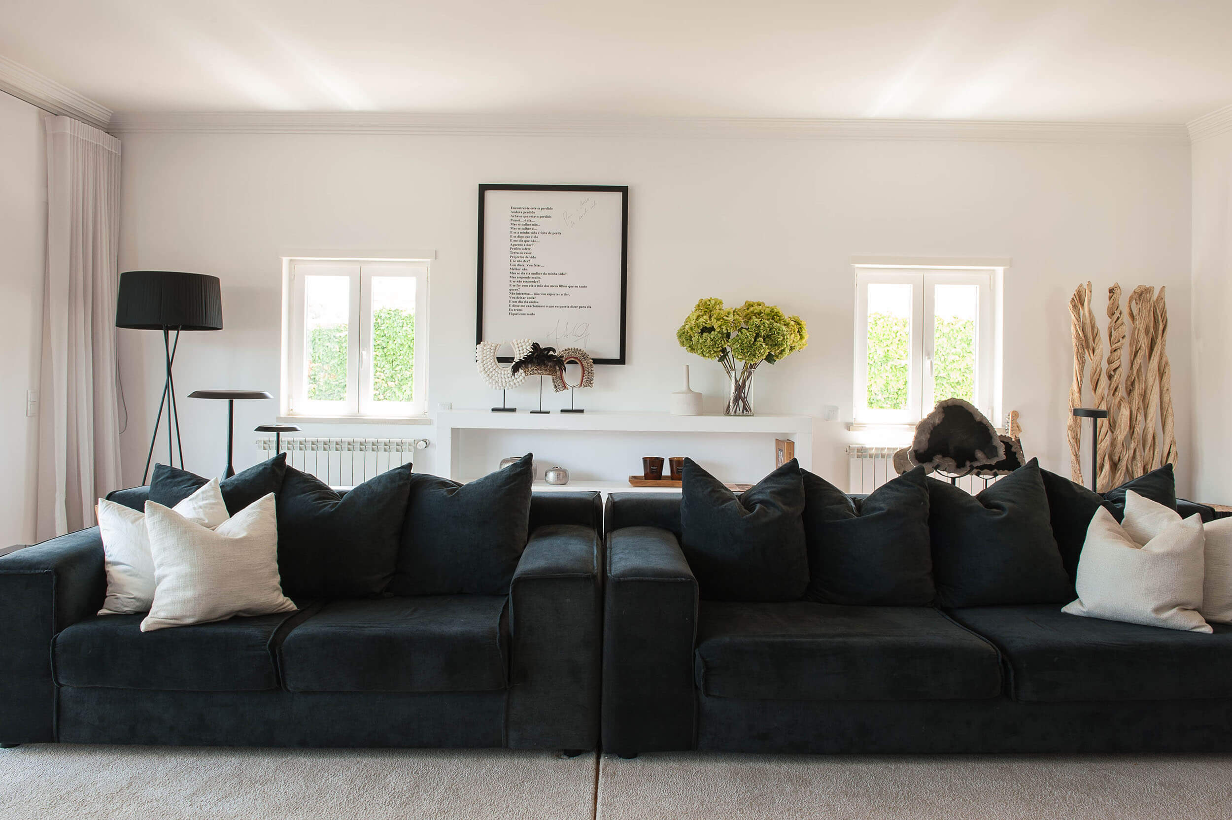 Deep navy velvet sofas, a framed poem artwork and a white console shelf with sculptural objects and driftwood — luxury living room