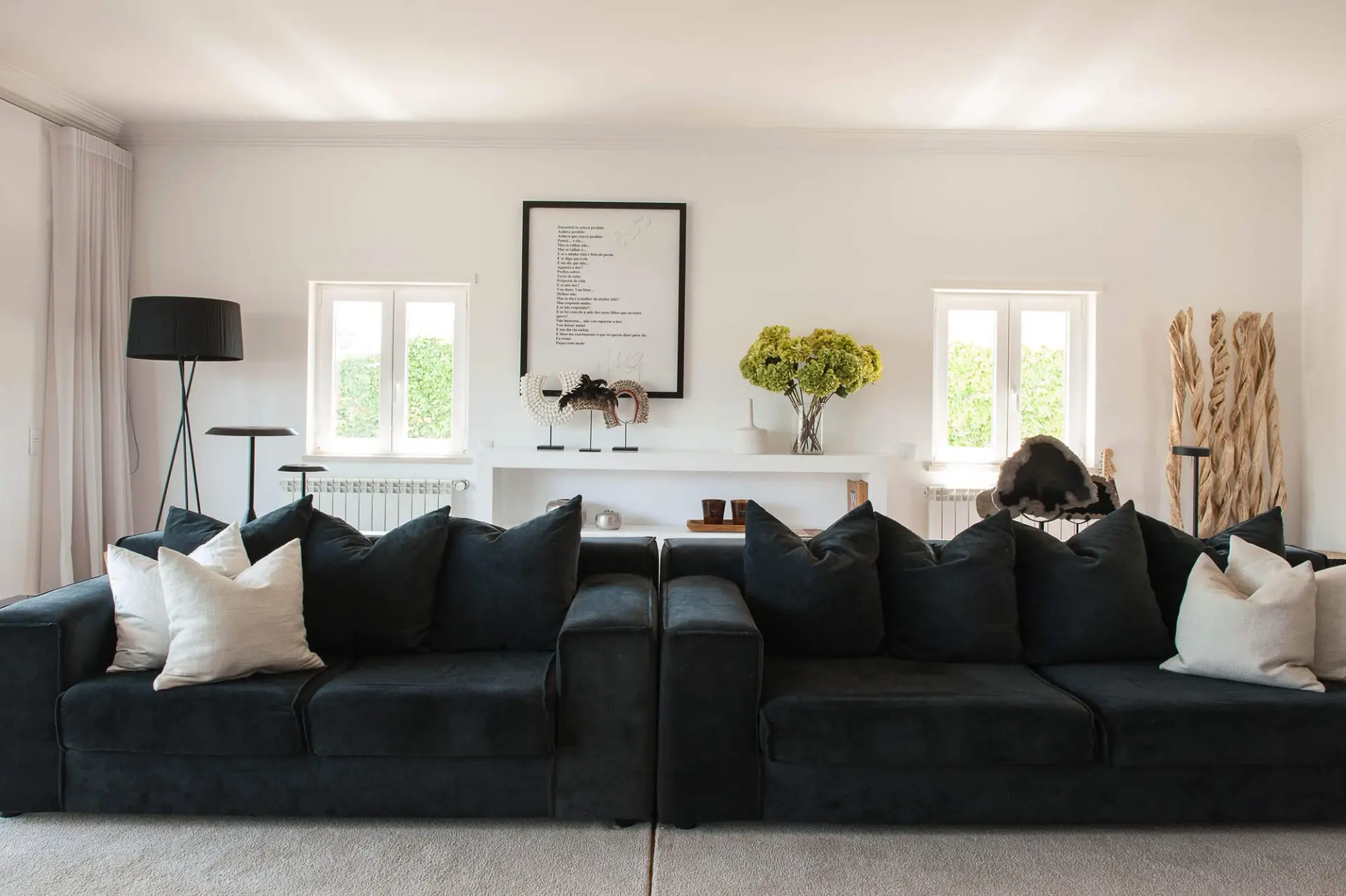 Deep navy velvet sofas, a framed poem artwork and a white console shelf with sculptural objects and driftwood — luxury living room