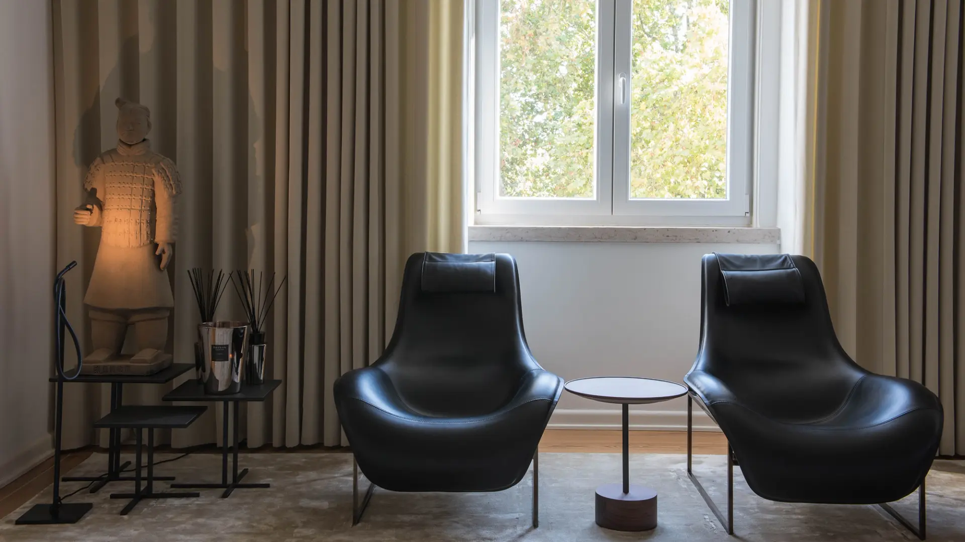Reading corner with two black armchairs, minimalist side table and natural light by the window