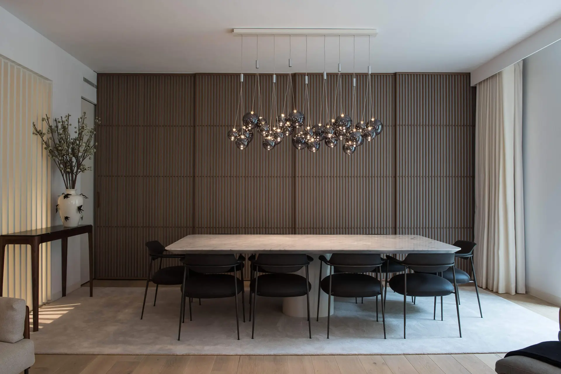 Swallow-motif vase on a walnut console, slatted oak wall and a smoked-glass sphere cluster pendant — luxury dining room