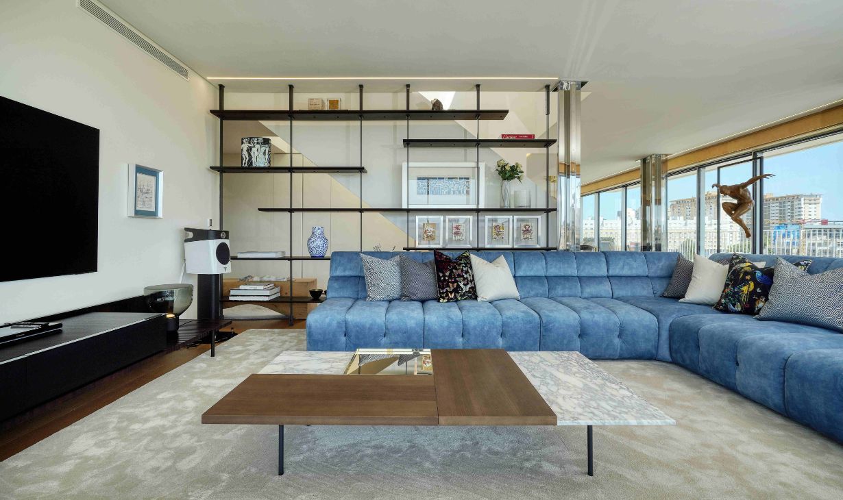 Contemporary living room interior design project in Lisbon by Atelier Renata Santos Machado, featuring a blue modular sofa, custom shelving and panoramic city views.
