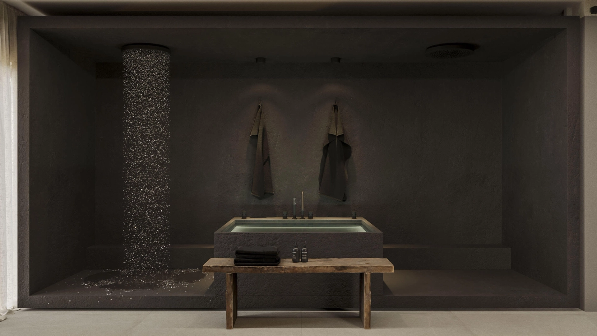 Recessed tub in dark microcement with a pebble shower column, a rustic wood bench and hanging towels — luxury bathroom