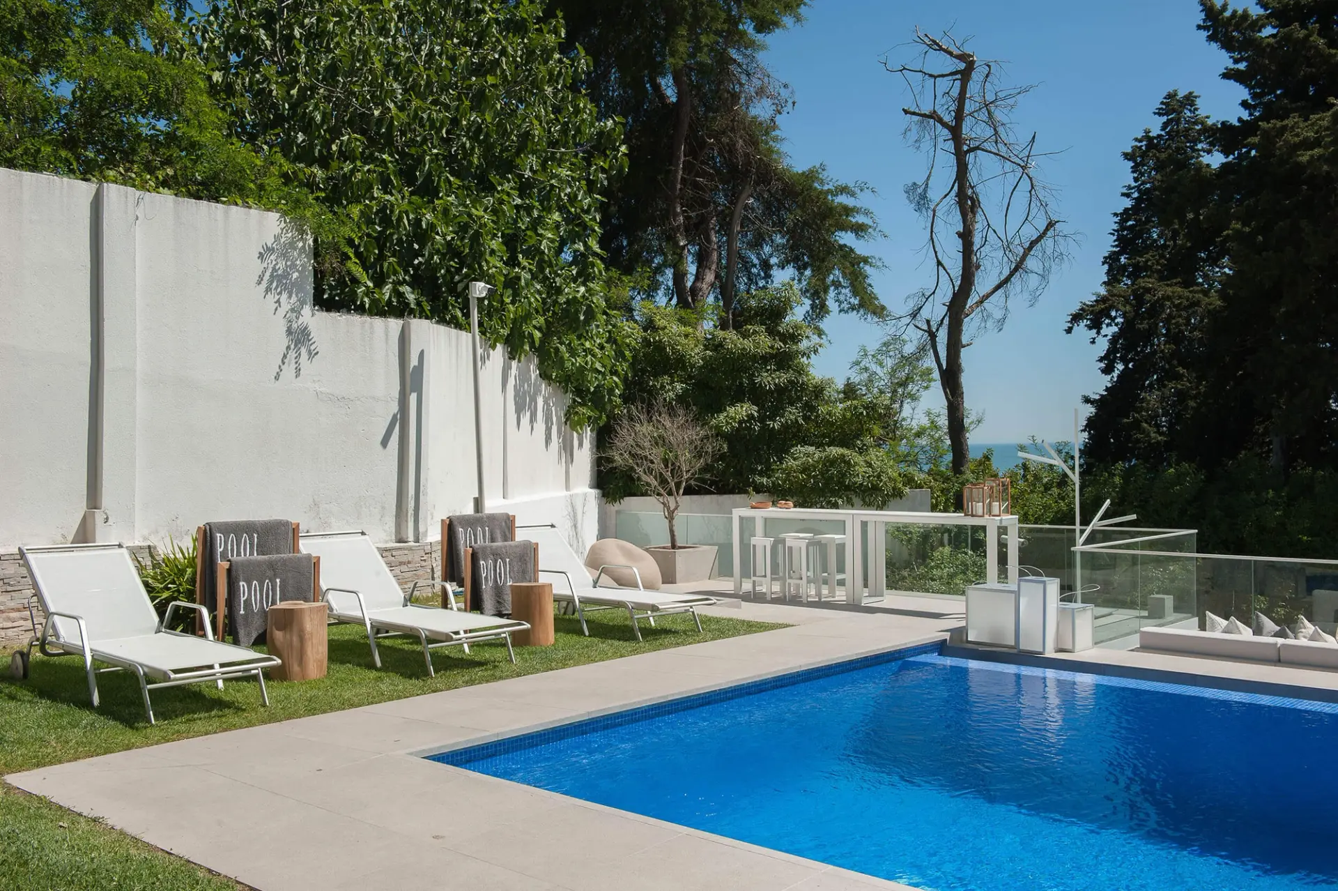 Piscina privada com espreguiçadeiras brancas, bancos Gloster LOG, relvado e vista mar — design de interiores de luxo Paço de Arcos, Oeiras, Atelier Renata Santos Machado