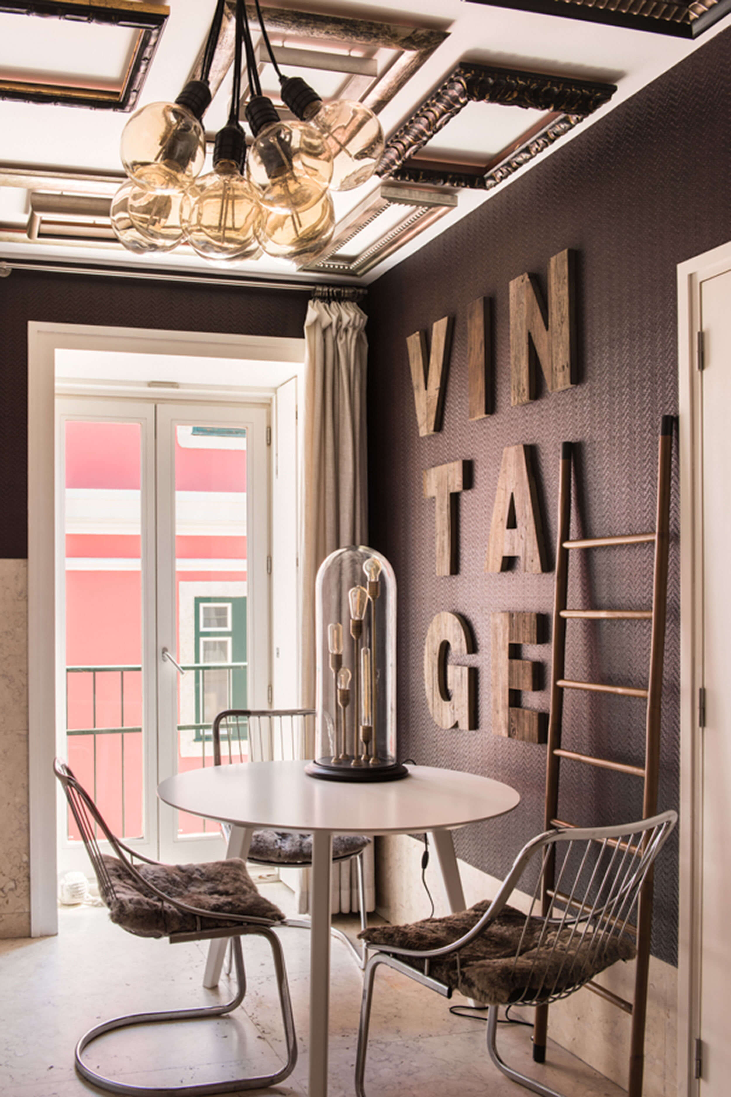 Wood 'VINTAGE' lettering on a charcoal wall, round table with wire chairs and a cluster of amber bulb pendants — luxury kitchen