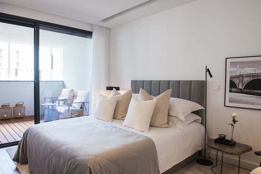 Quarto contemporâneo preparado para homestaging com cama estofada, tons neutros, iluminação suave e varanda exterior.