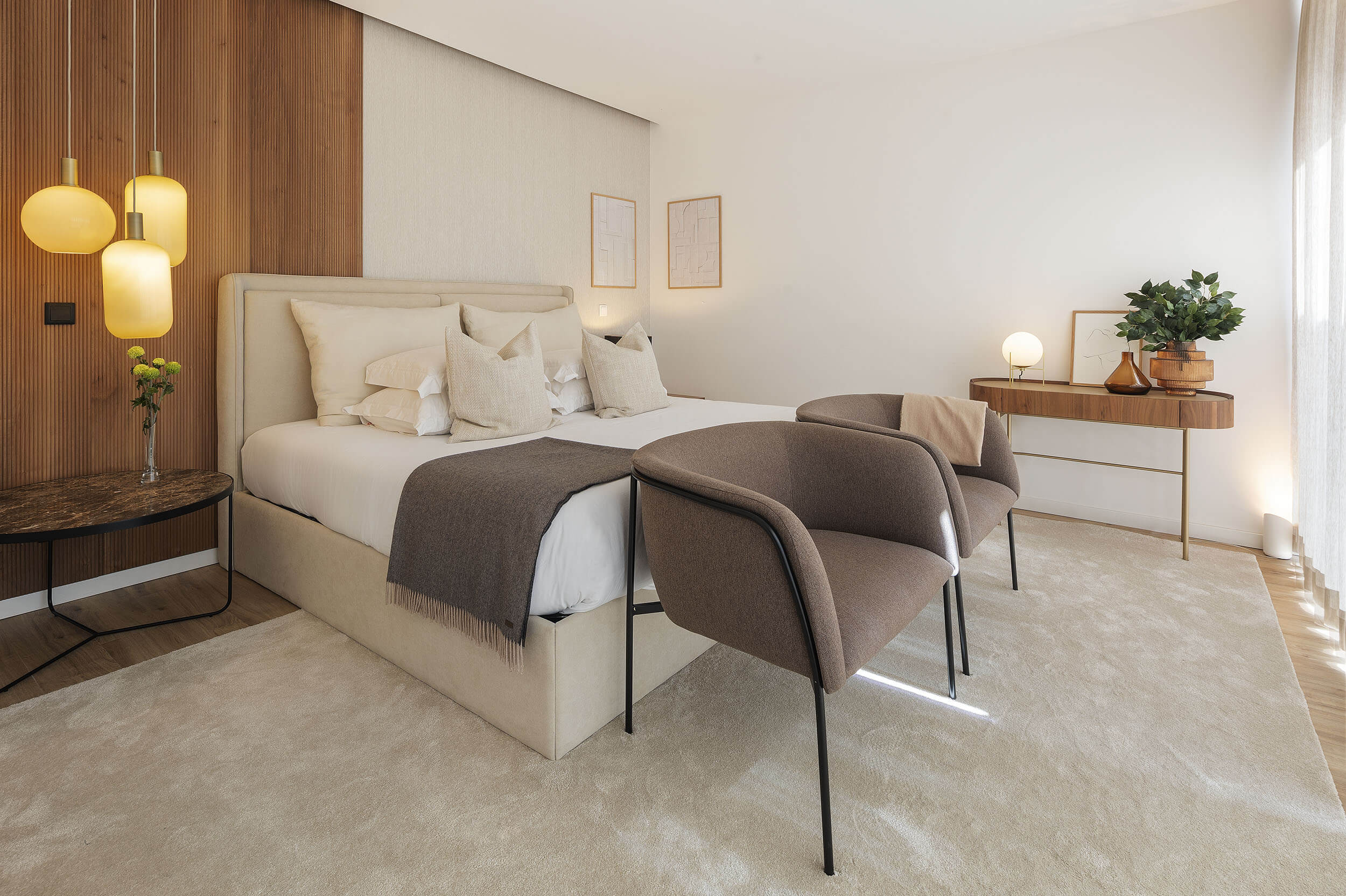 Beige upholstered headboard, amber glass pendant cluster and bouclé armchairs against a wood-slat wall — luxury master suite design