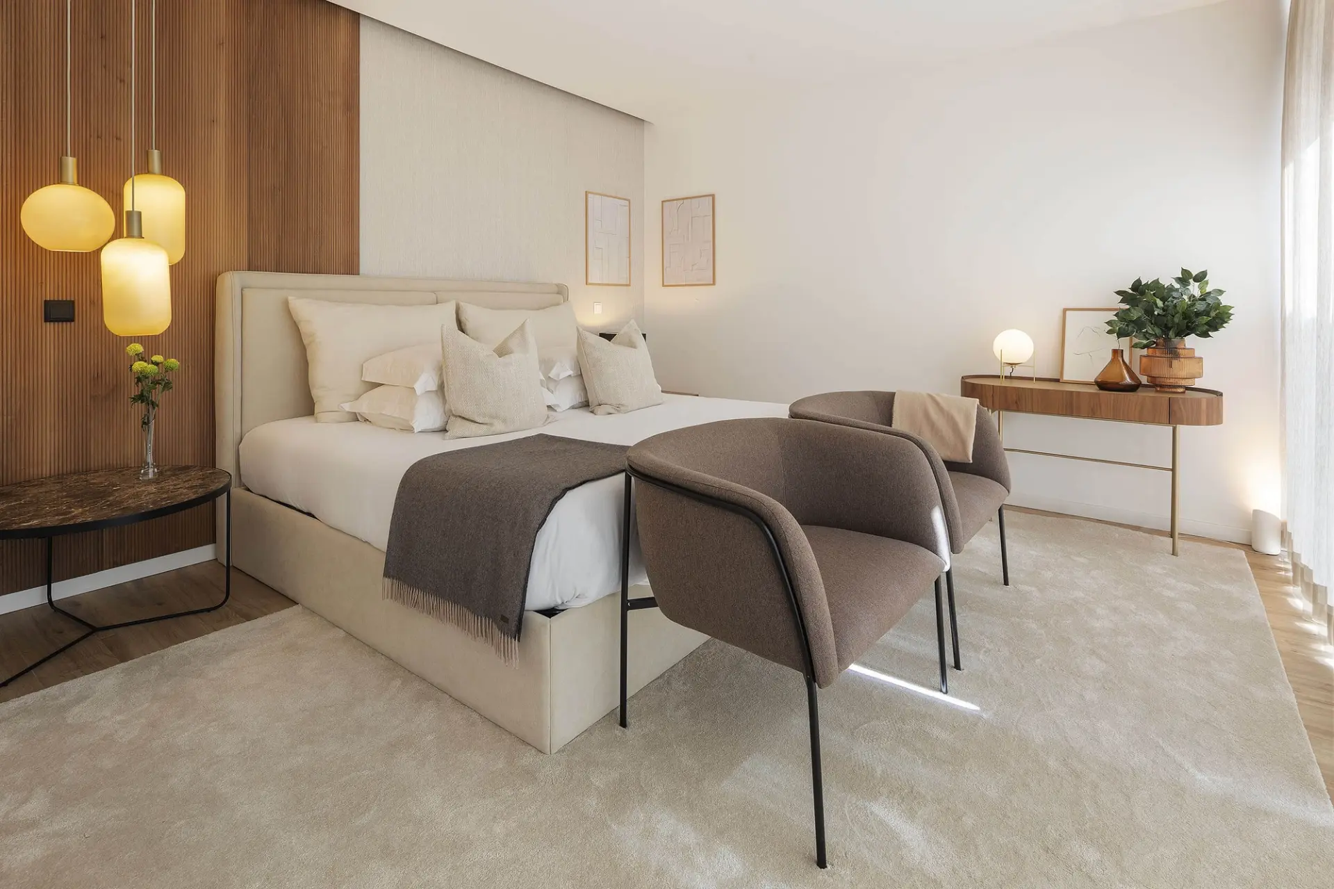 Beige upholstered headboard, amber glass pendant cluster and bouclé armchairs against a wood-slat wall — luxury master suite design