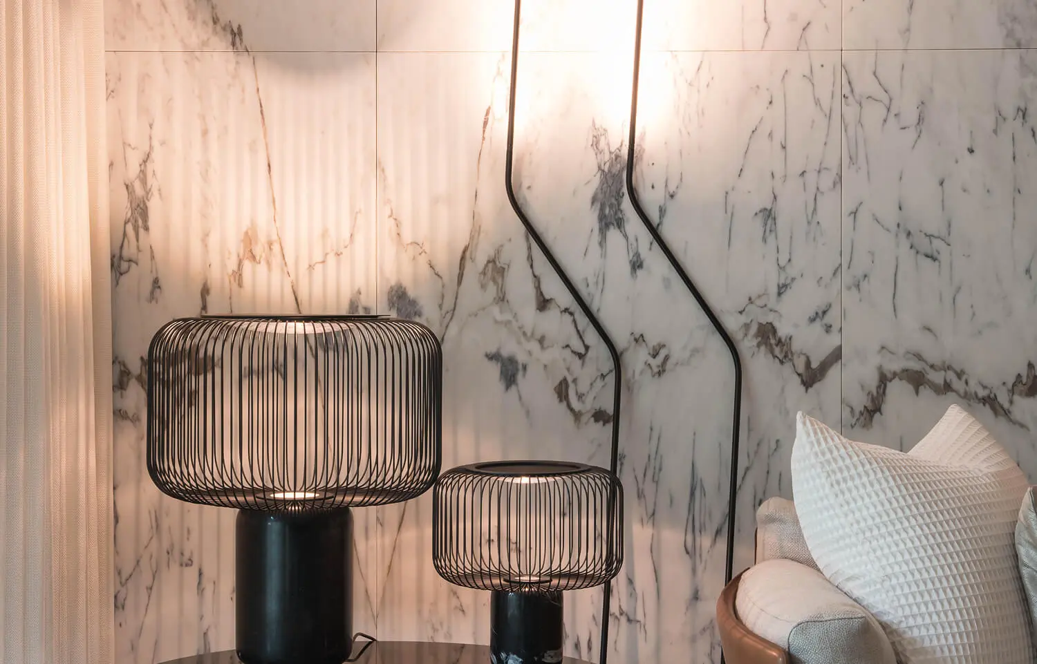 Elegant living room corner with a marble wall, black metal side tables and a sculptural black iron floor lamp.