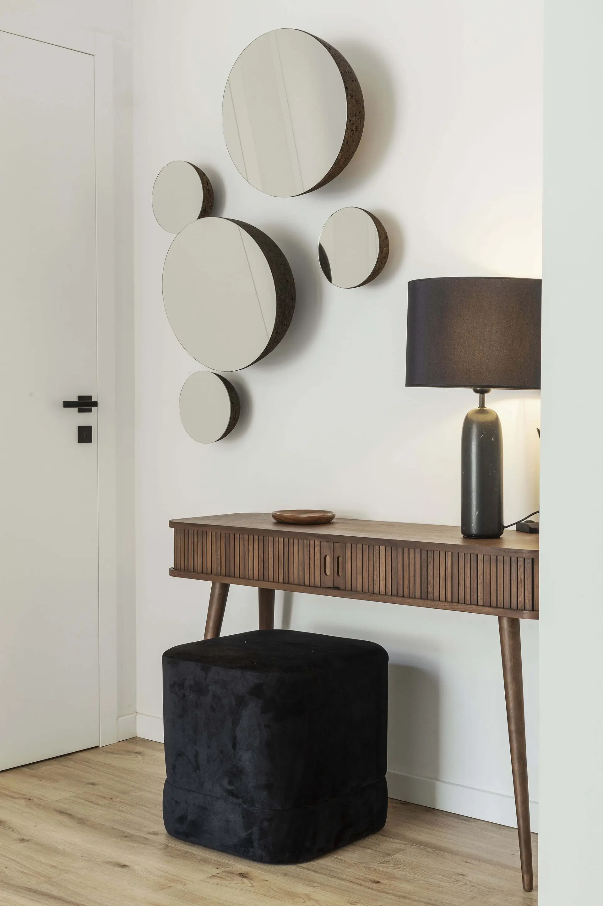 Reeded walnut console, a cluster of round wall mirrors and a black dome table lamp above a velvet cube pouf — luxury entrance hall