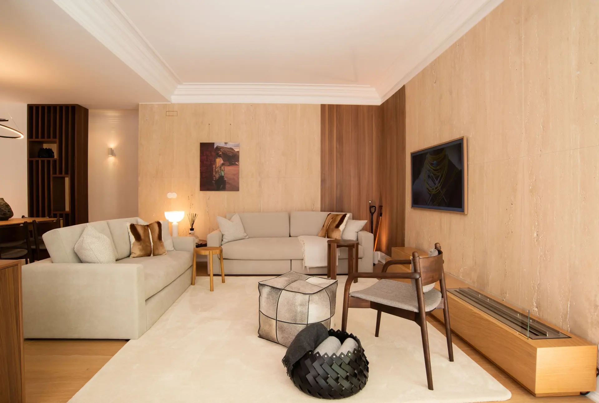 Travertine walls, sage-green sofas, a cowhide cube pouf and an African-themed photograph by a wood-clad fireplace — luxury living room