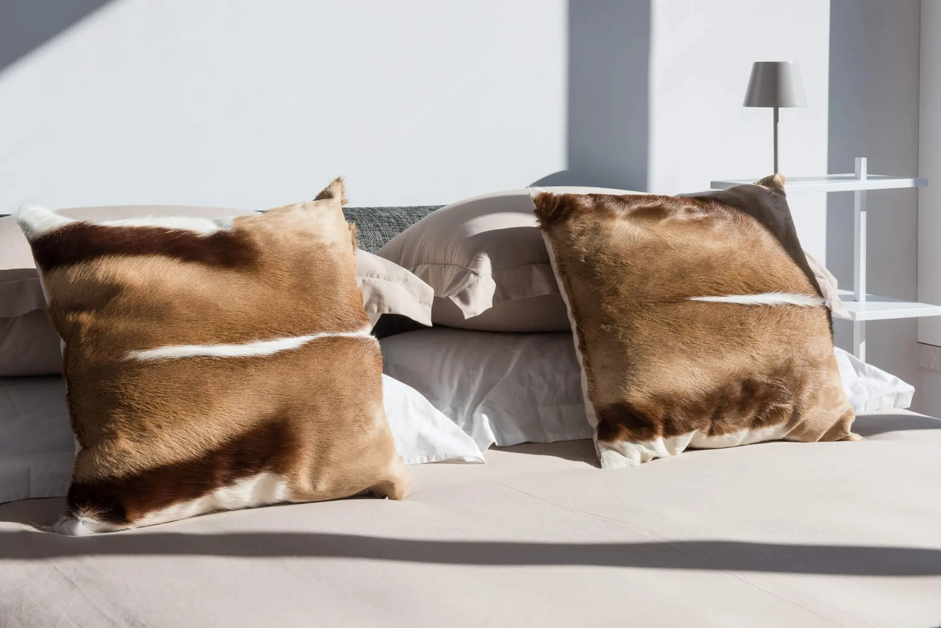 Detalhe de cama de suite com almofadas Mambo em pelo de gazela e roupa de cama em linho creme — design de interiores de luxo, Lisboa, Atelier Renata Santos Machado