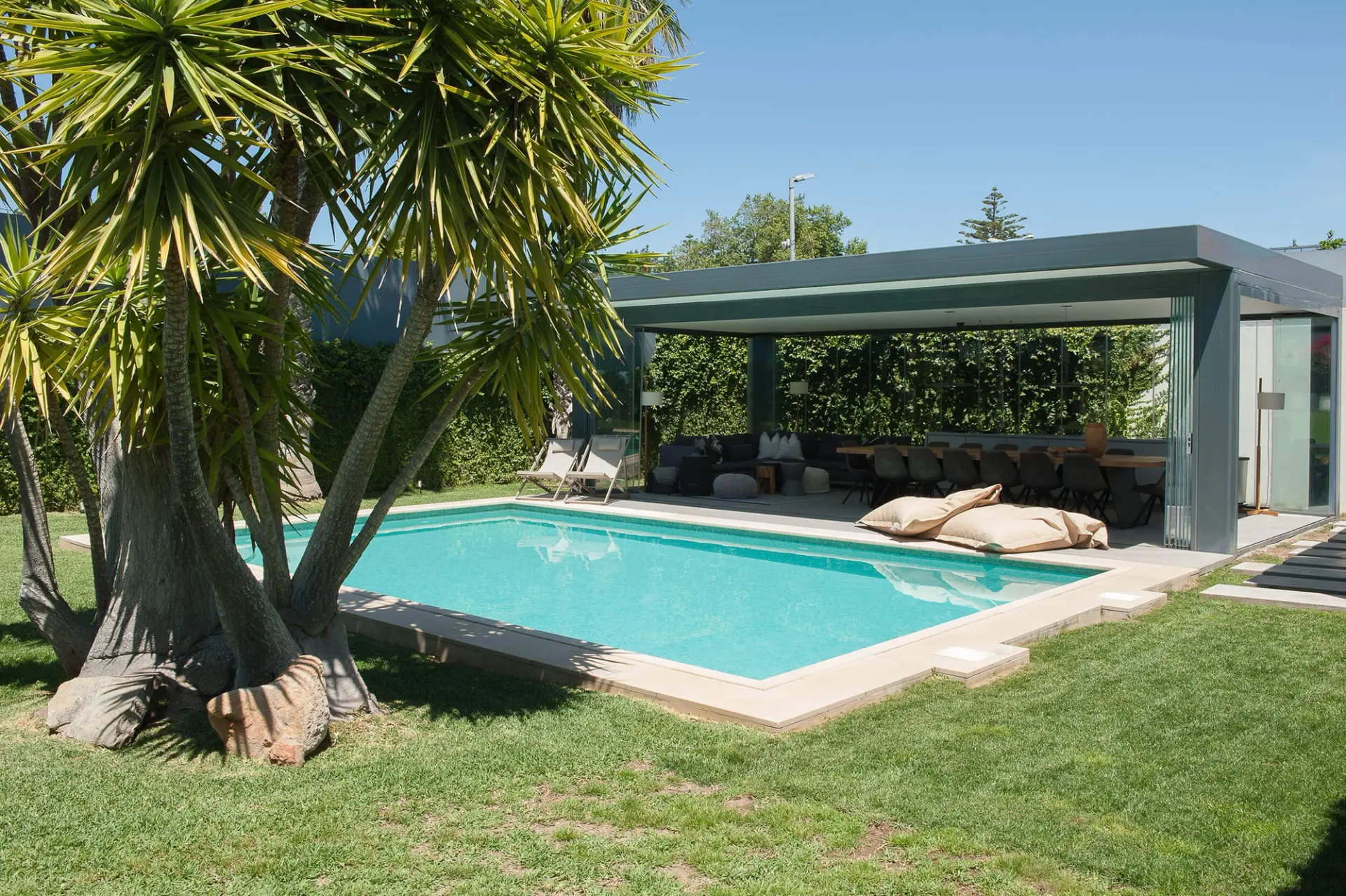 Piscina retangular com revestimento de mosaico, alpendre envidraçado com zona de refeições e palmeira em destaque — exterior de luxo