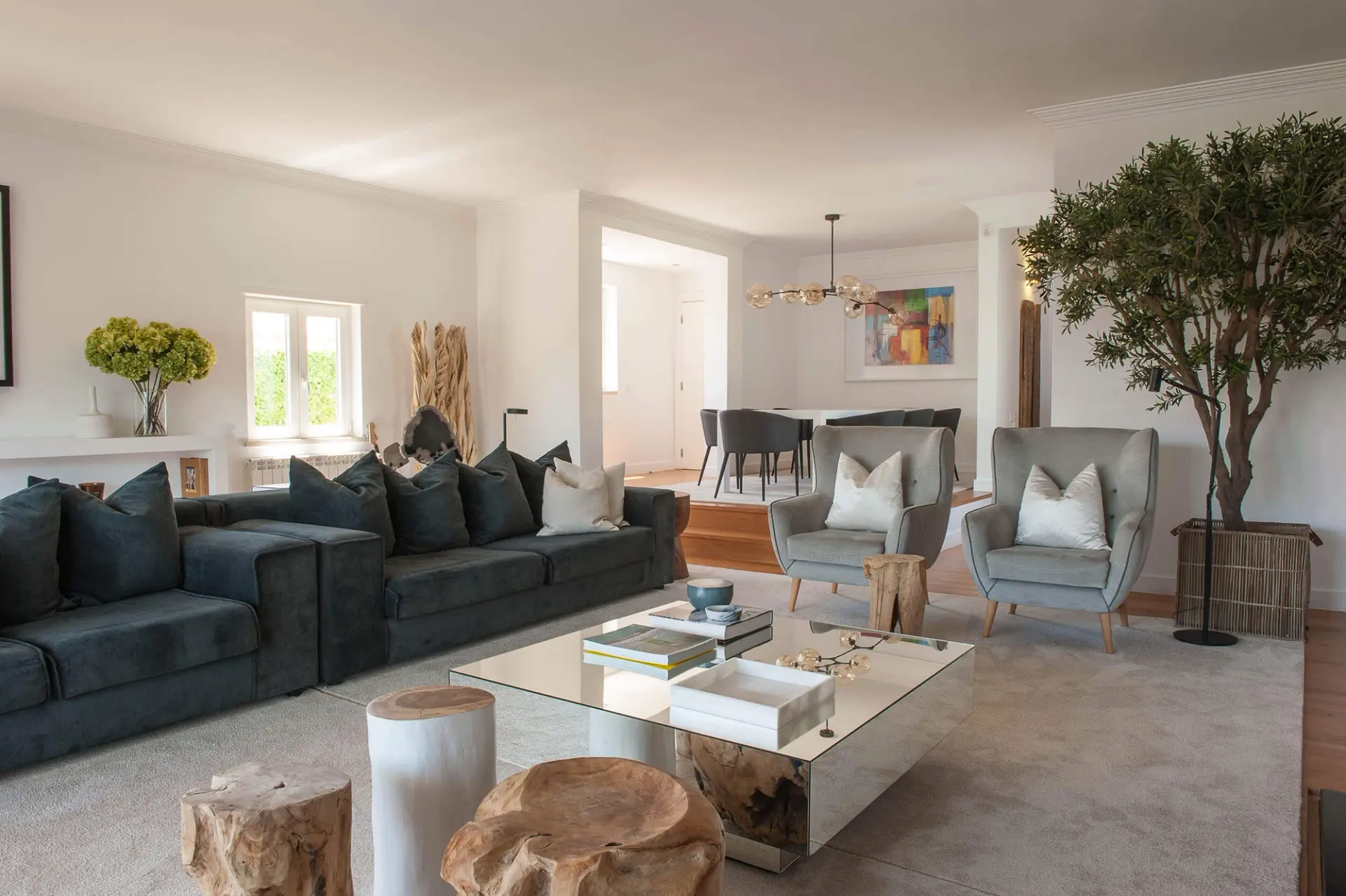 Grey wingback armchairs, a glass-globe chandelier and colourful abstract artwork beside a mirrored coffee table — luxury living room
