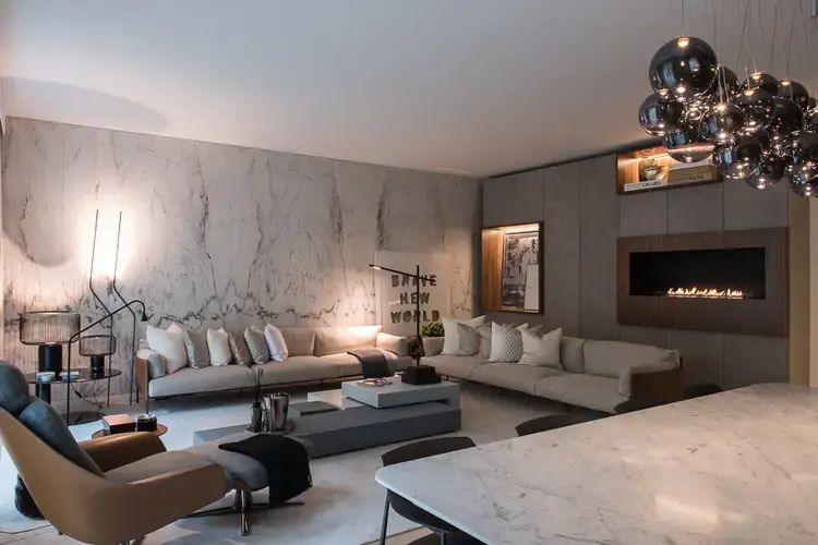 Living room with beige sofas, layered coffee tables, decorative lamps, and a cluster of metallic pendant lights.