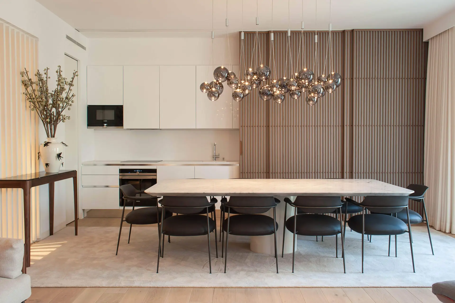 White Carrara marble table, black leather chairs and a smoked-glass sphere cluster above an open kitchen — luxury dining room
