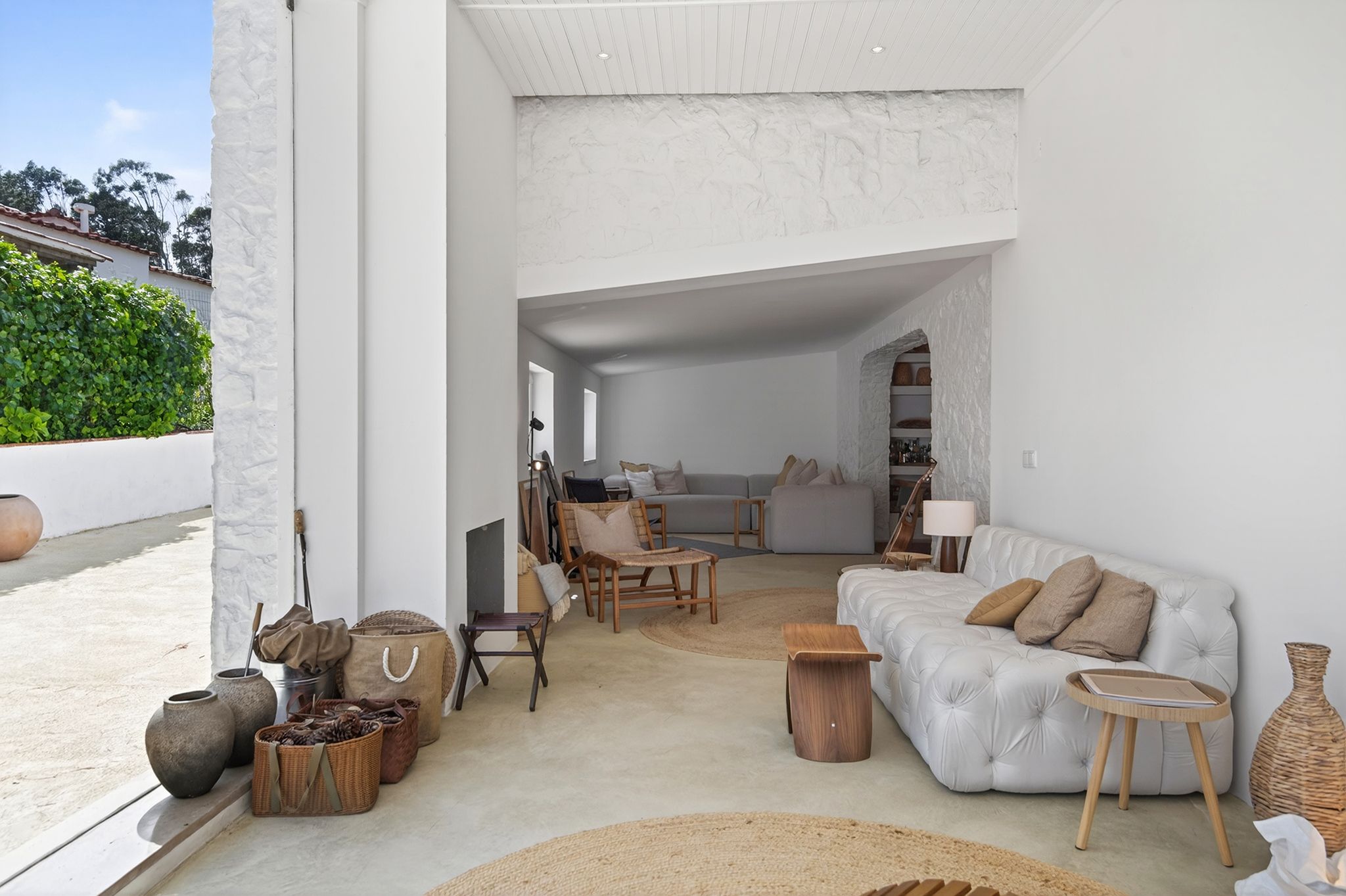 Sala de estar com sofá branco capitoné, poltronas de madeira, tapetes de fibra natural e abertura para o pátio, no Bom Sucesso.