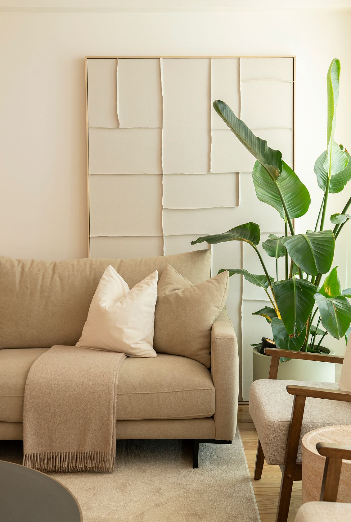 Cream textured relief wall art, beige sofa with black legs and bouclé armchair with wooden arms — luxury décor details
