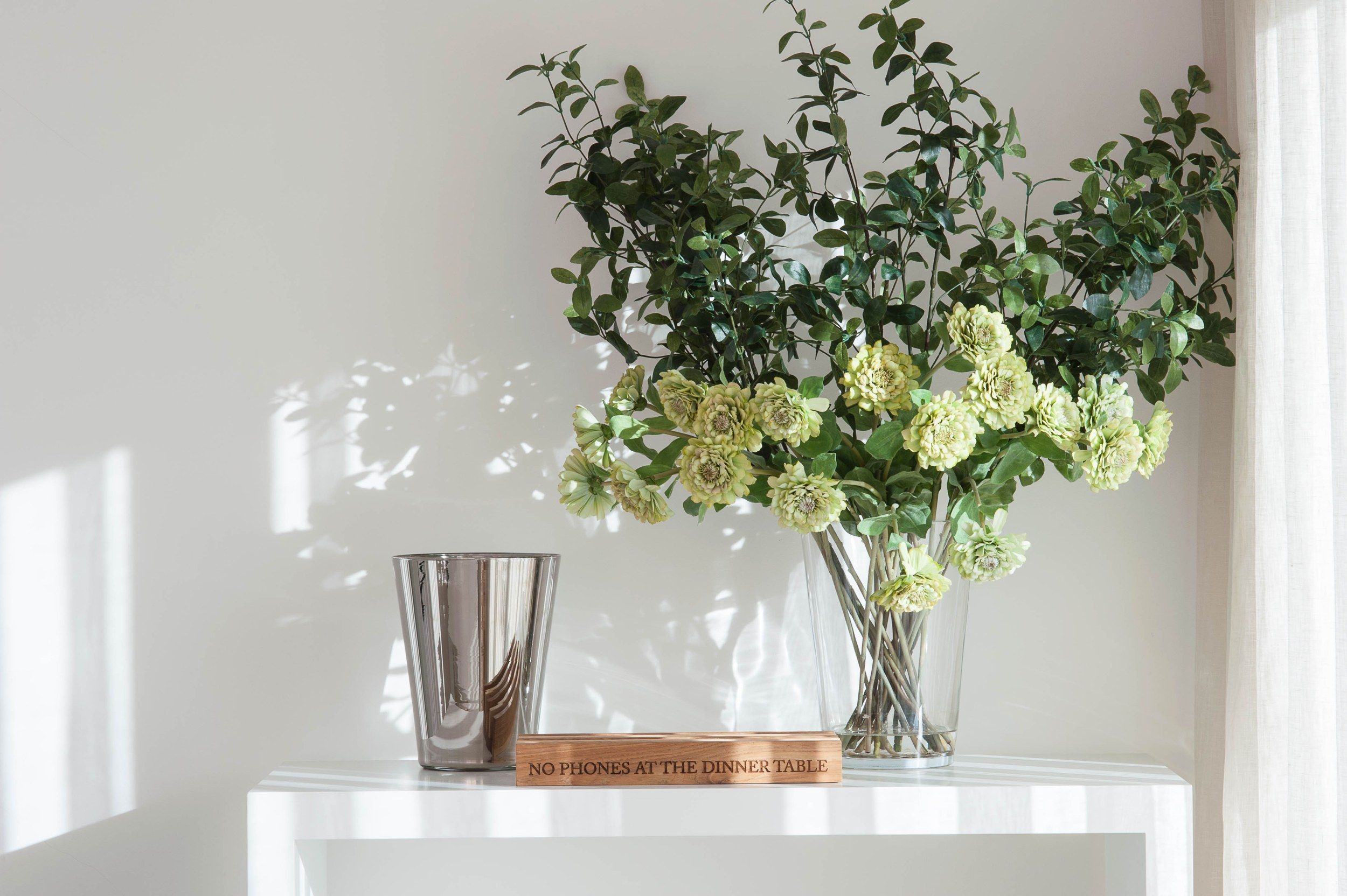 White console with flowers and a metal vase in daylight