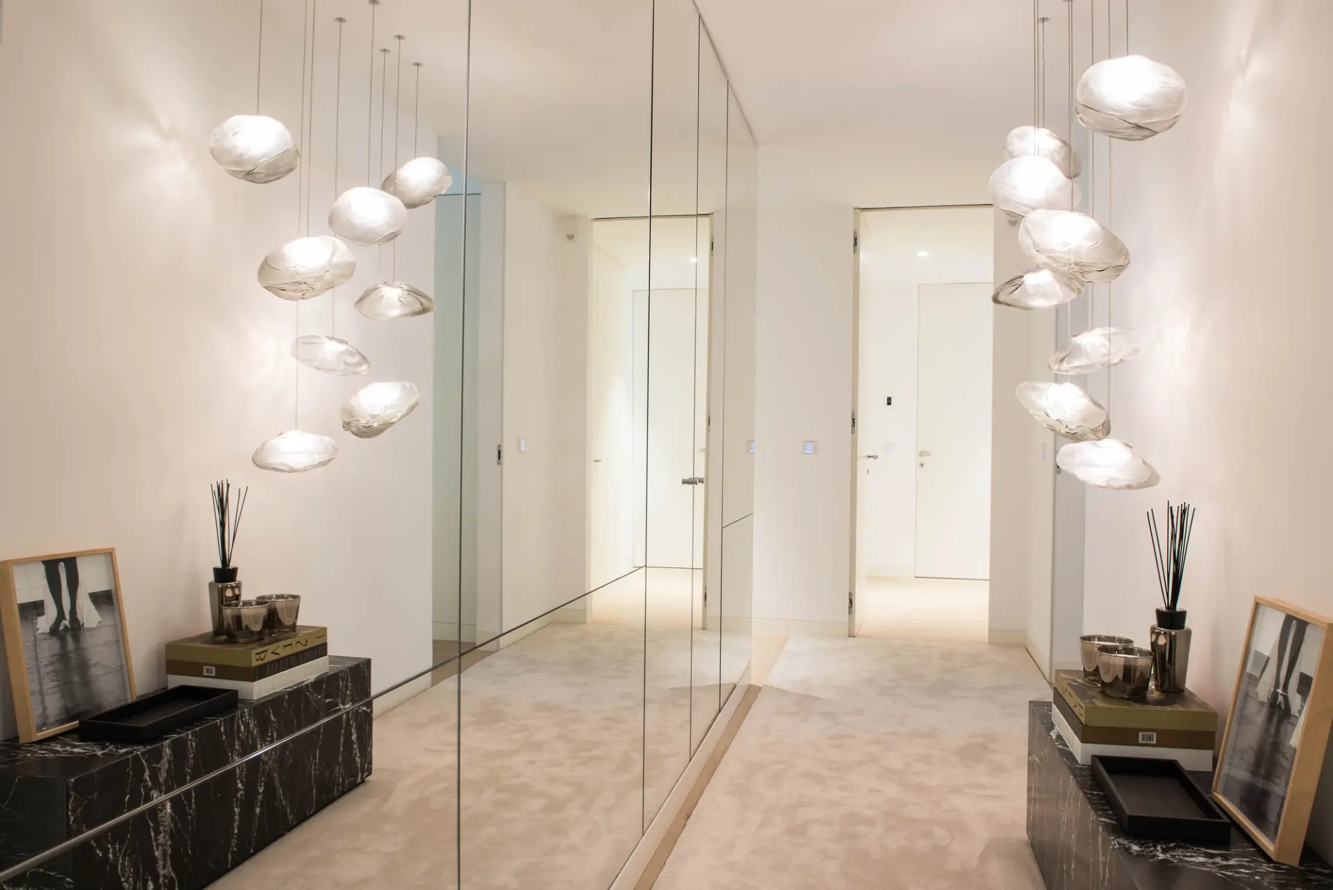 Hall de entrada de apartamento remodelado em Lisboa, com parede espelhada, iluminação suspensa e consola em pedra.