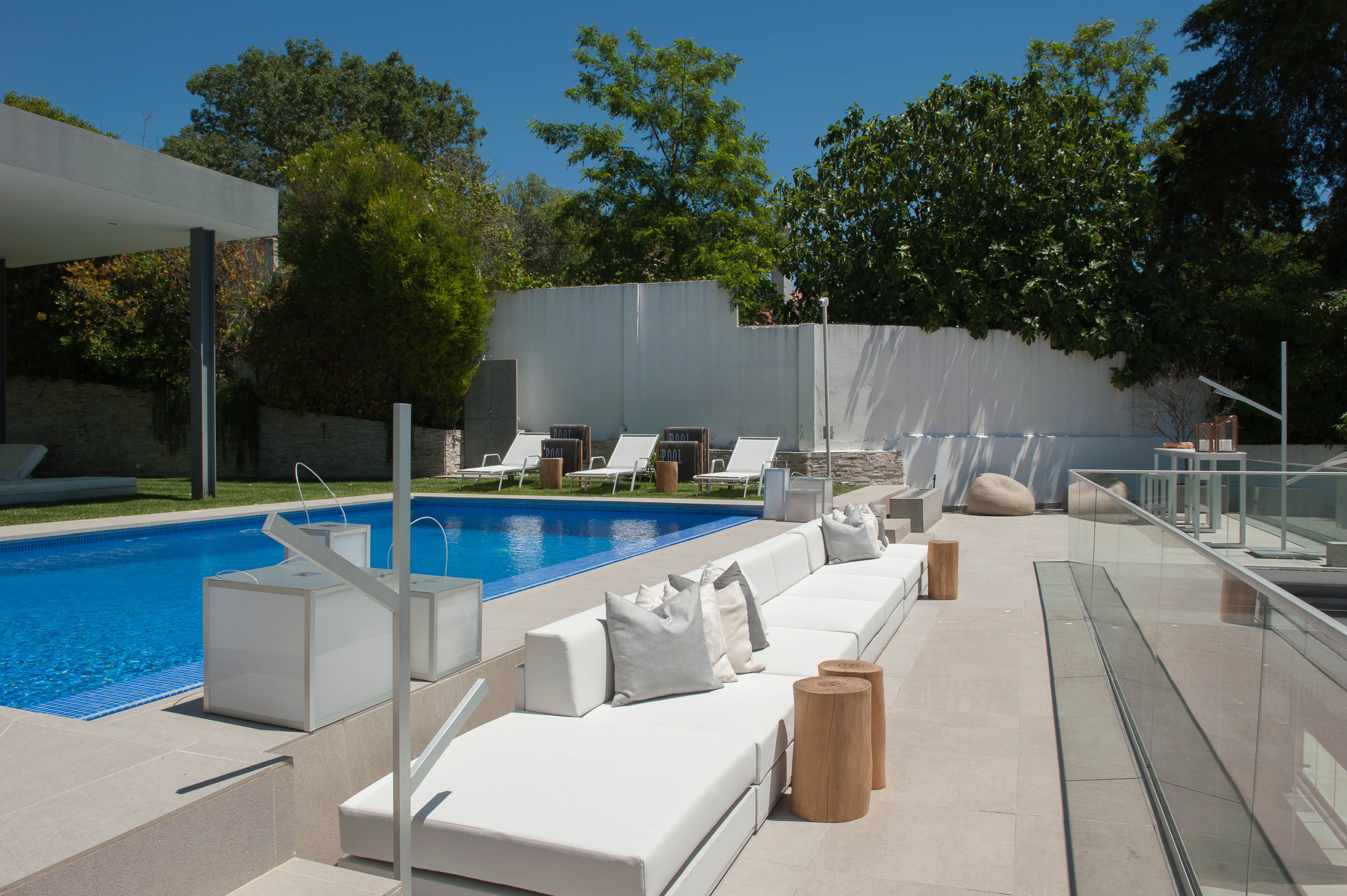 Área exterior contemporânea em moradia no Algarve com piscina, lounge branco, pedra natural e zonas de estar pensadas para o clima costeiro.